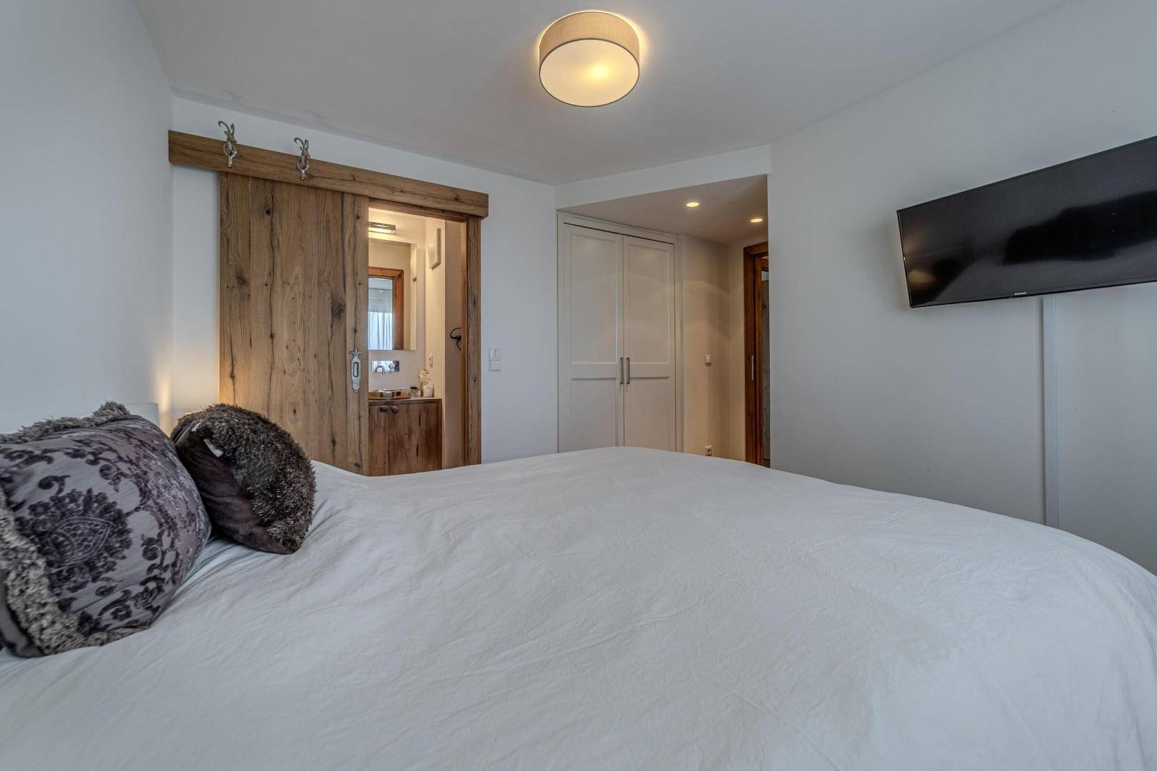 Schlafzimmer mit Holzboden und Schiebetür, die zu einem modernen Badezimmer führt.