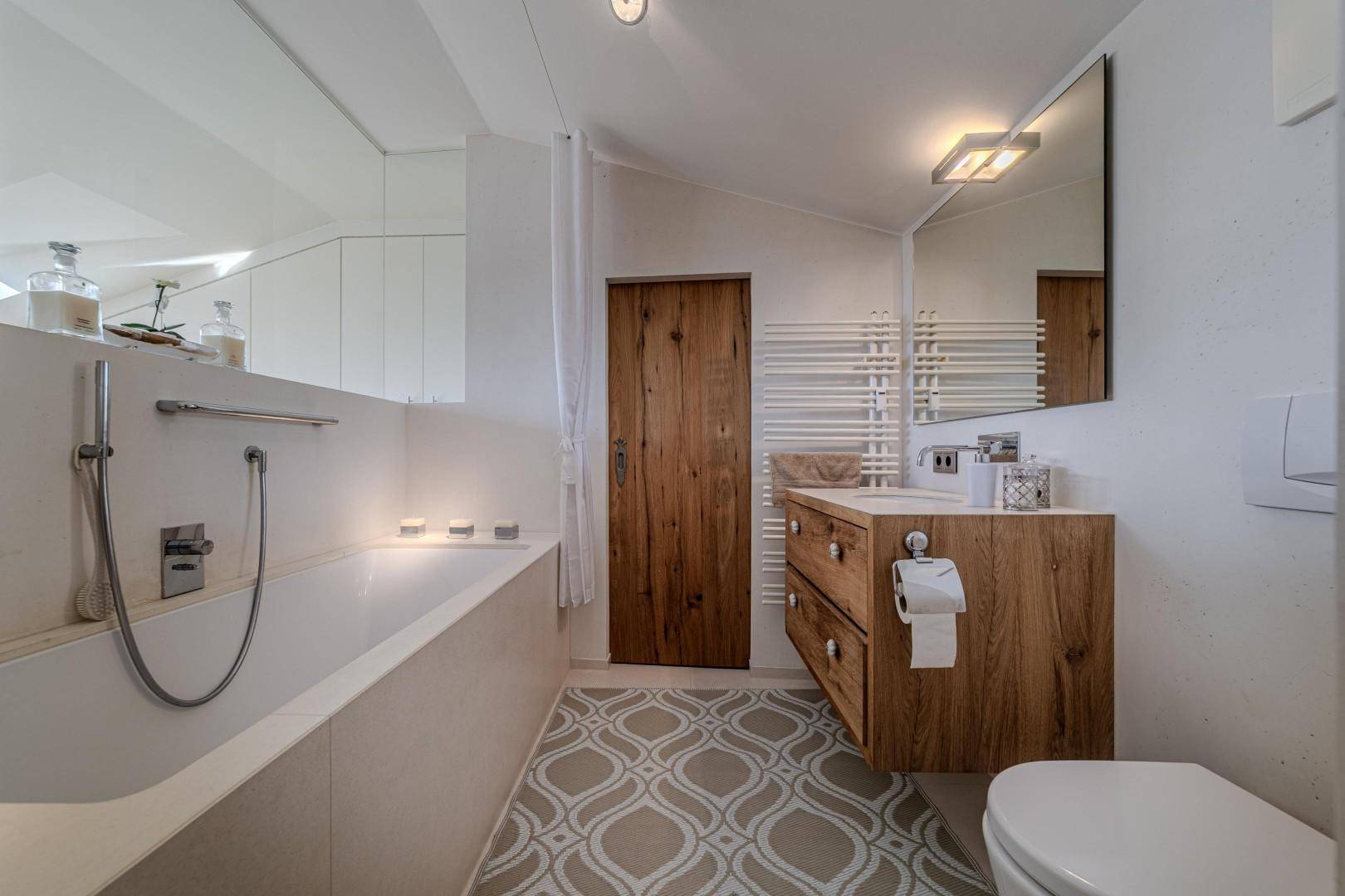 Modernes Badezimmer mit Badewanne, Holzwaschtisch und gemusterten Fliesen auf dem Boden.