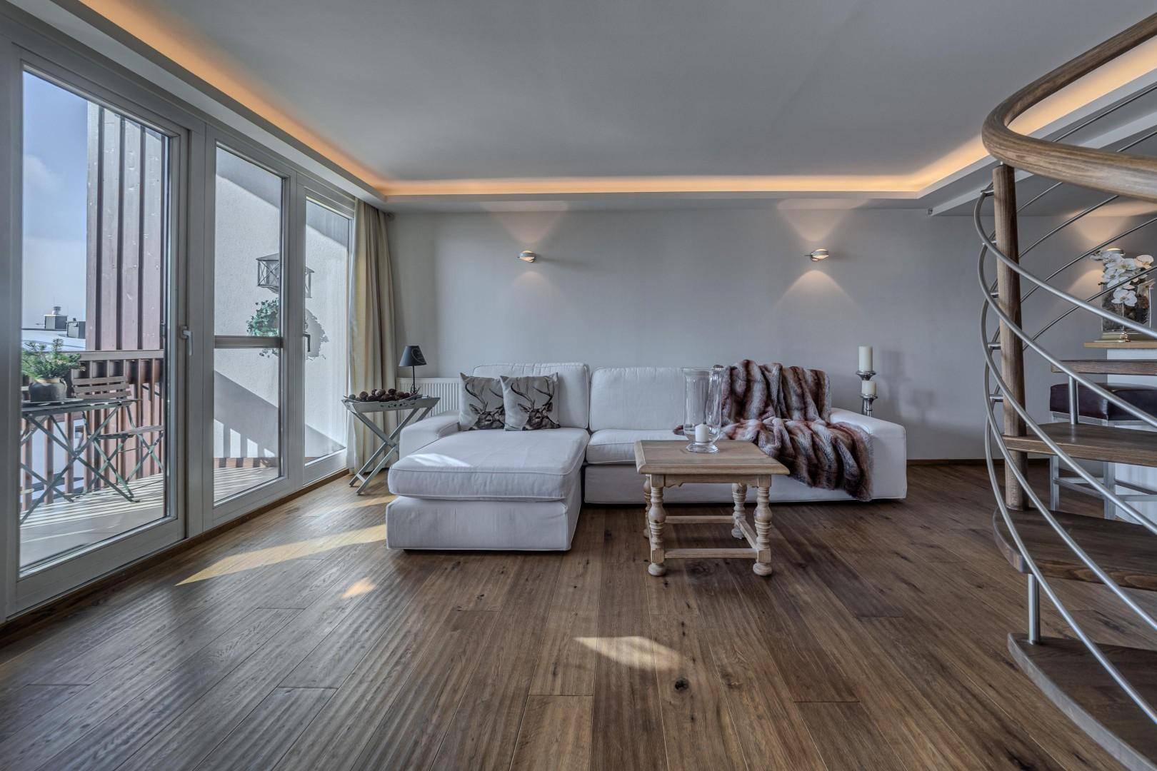 Helles Wohnzimmer mit weißem Sofa, Holzboden und großen Fenstern, die auf einen Balkon führen.