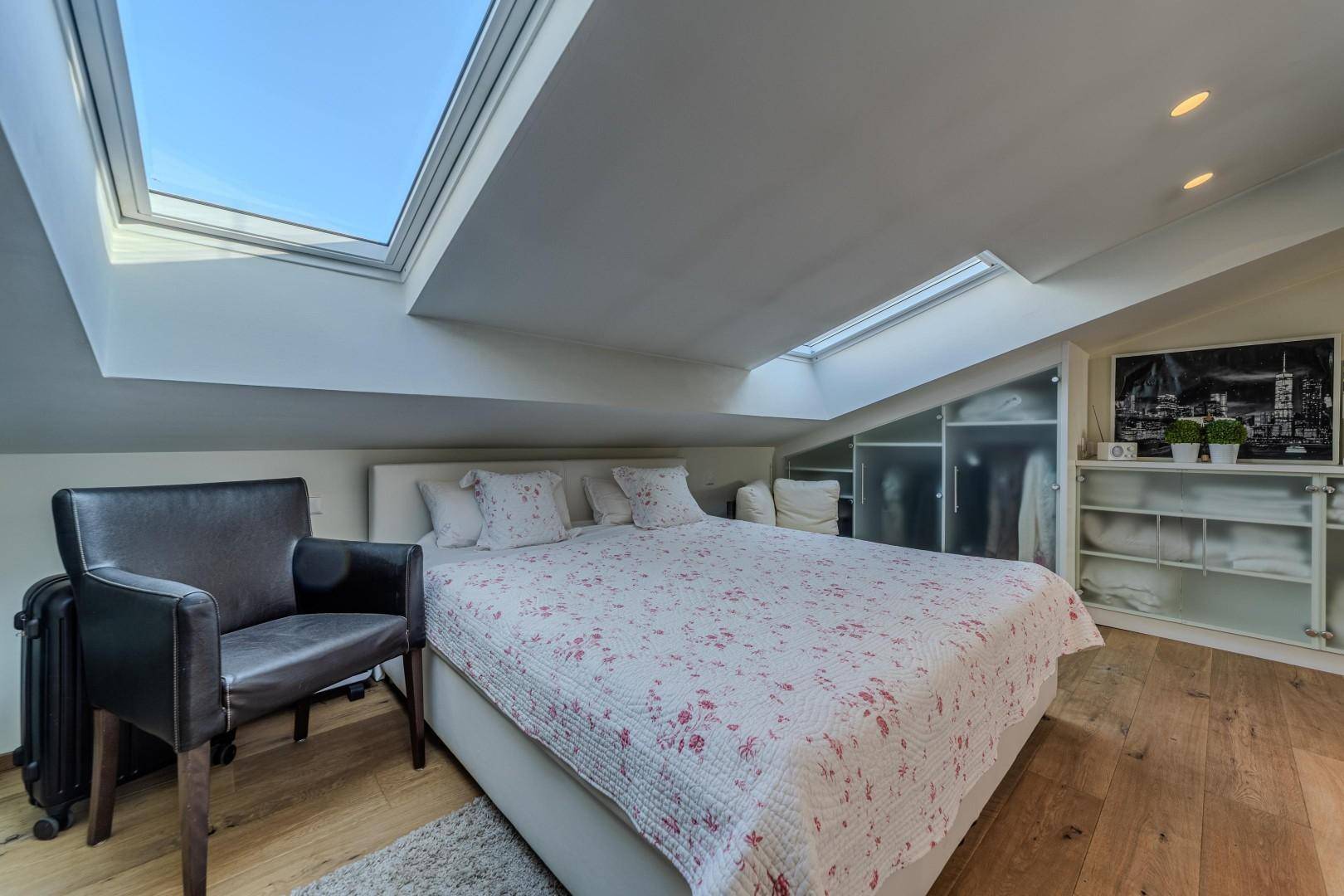 Helles Schlafzimmer mit Holzboden, integrierten Schränken und großzügigen Dachfenstern.