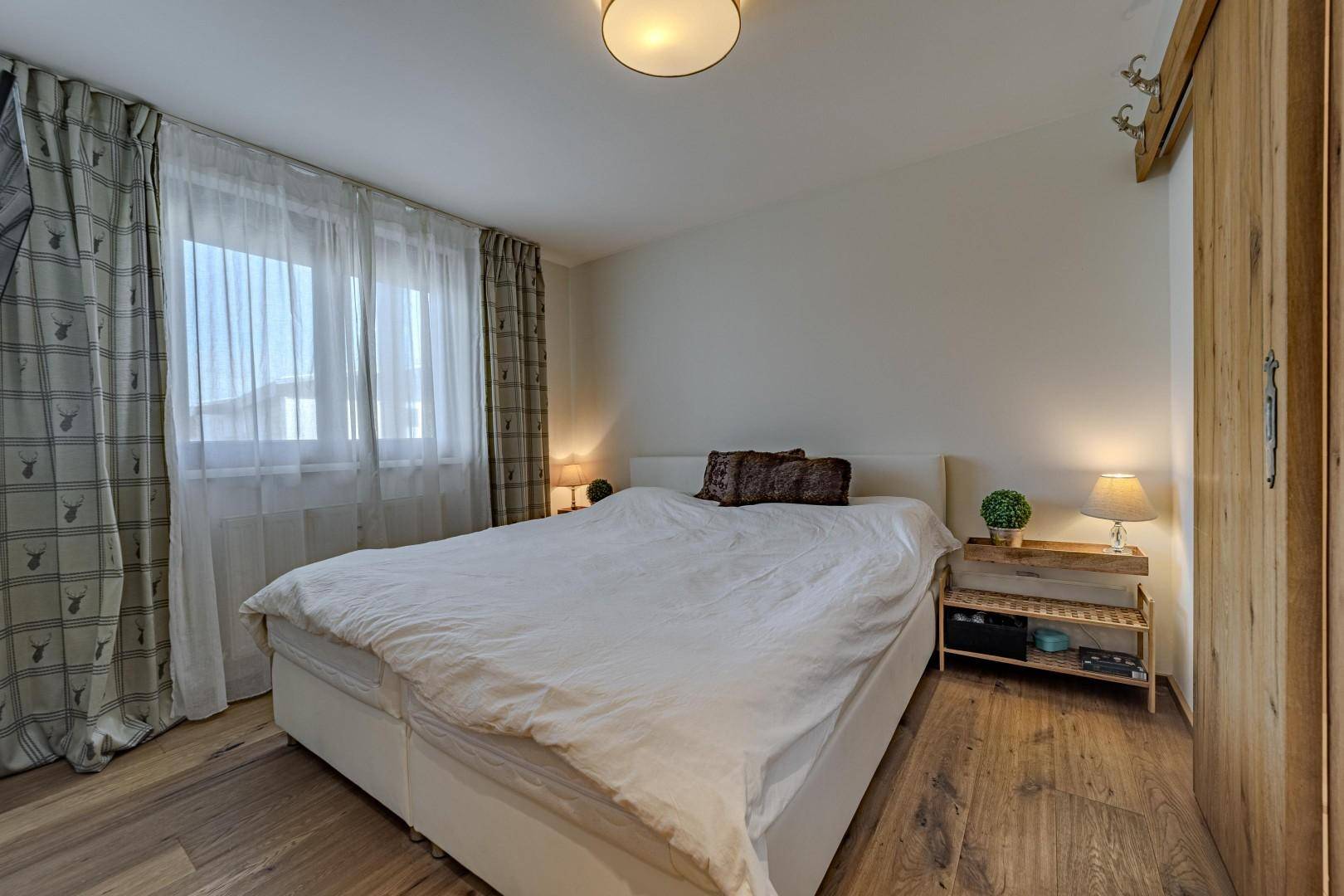 Gemütliches Schlafzimmer mit Doppelbett, Holzboden und großen Fenstern mit Vorhängen.