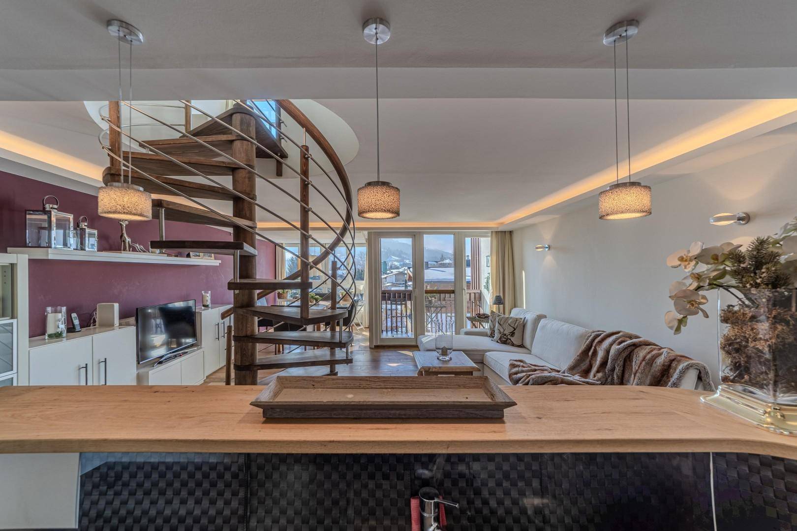 Offener Wohnbereich mit Küche, Wendeltreppe und Zugang zu einem sonnigen Balkon.
