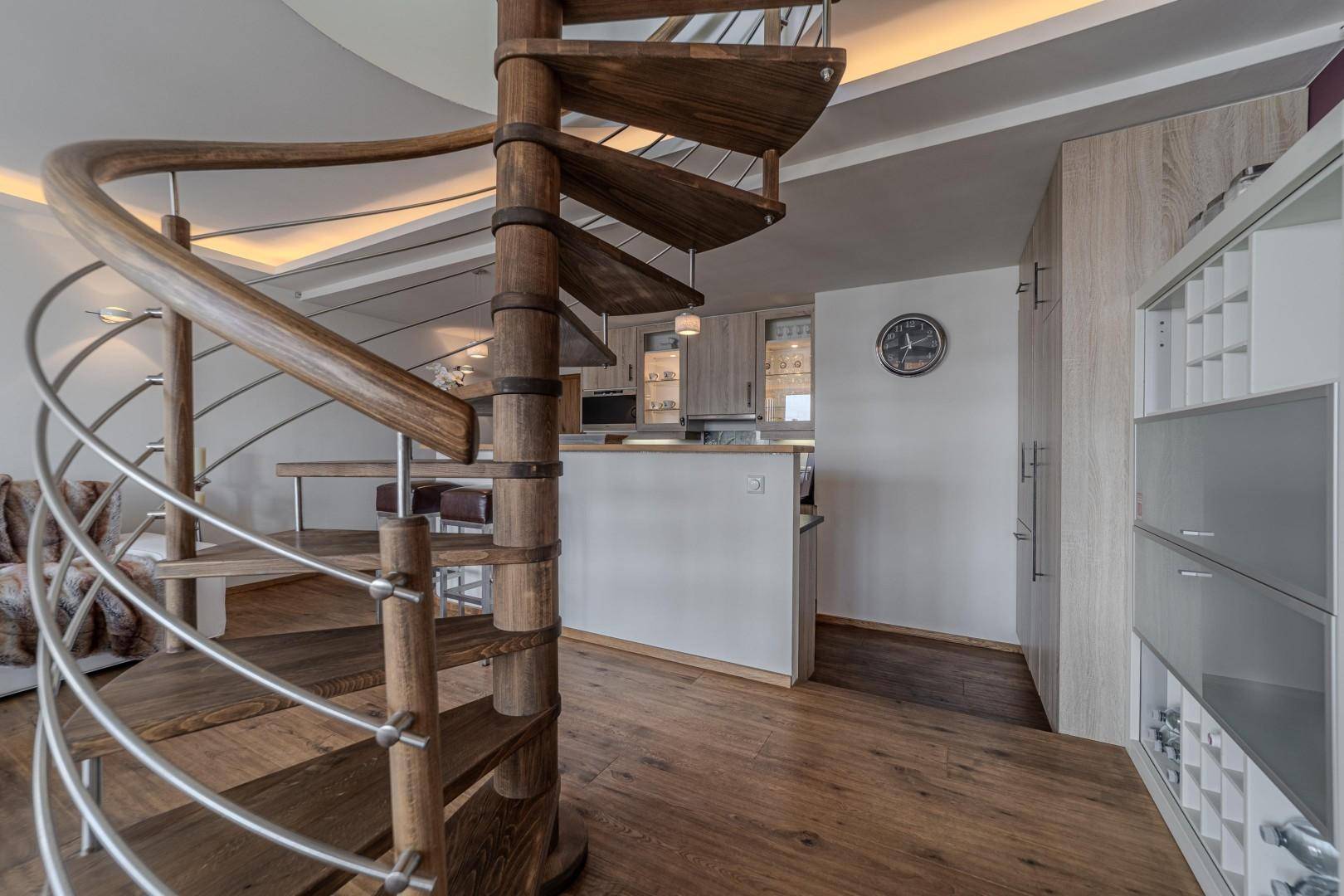 Offene Küche mit Holzfronten und dunkler Arbeitsplatte, direkt neben der eleganten Wendeltreppe.