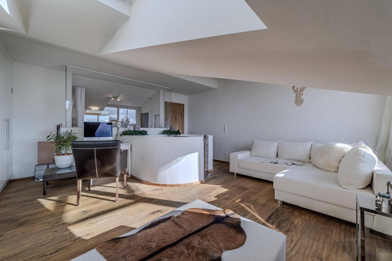 Geräumiges Wohnzimmer im Dachgeschoss mit Holzboden, weißem Sofa und modernem Arbeitsbereich.