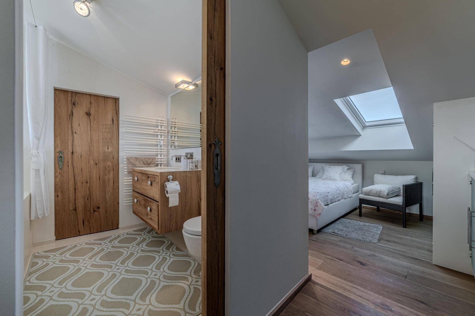 Badezimmer mit Holztür und Blick auf das angrenzende Schlafzimmer im Dachgeschoss.