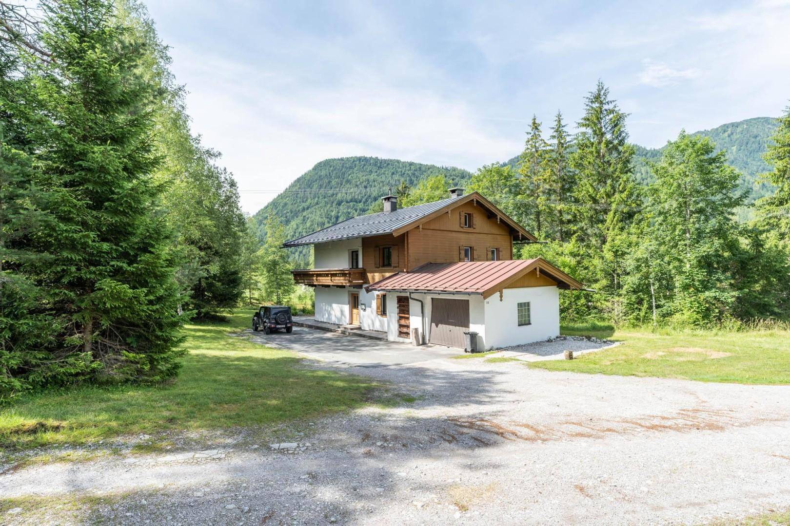 Traditionelles Haus mit Anbau und Garage, umgeben von Bäumen und einer Schotterauffahrt.