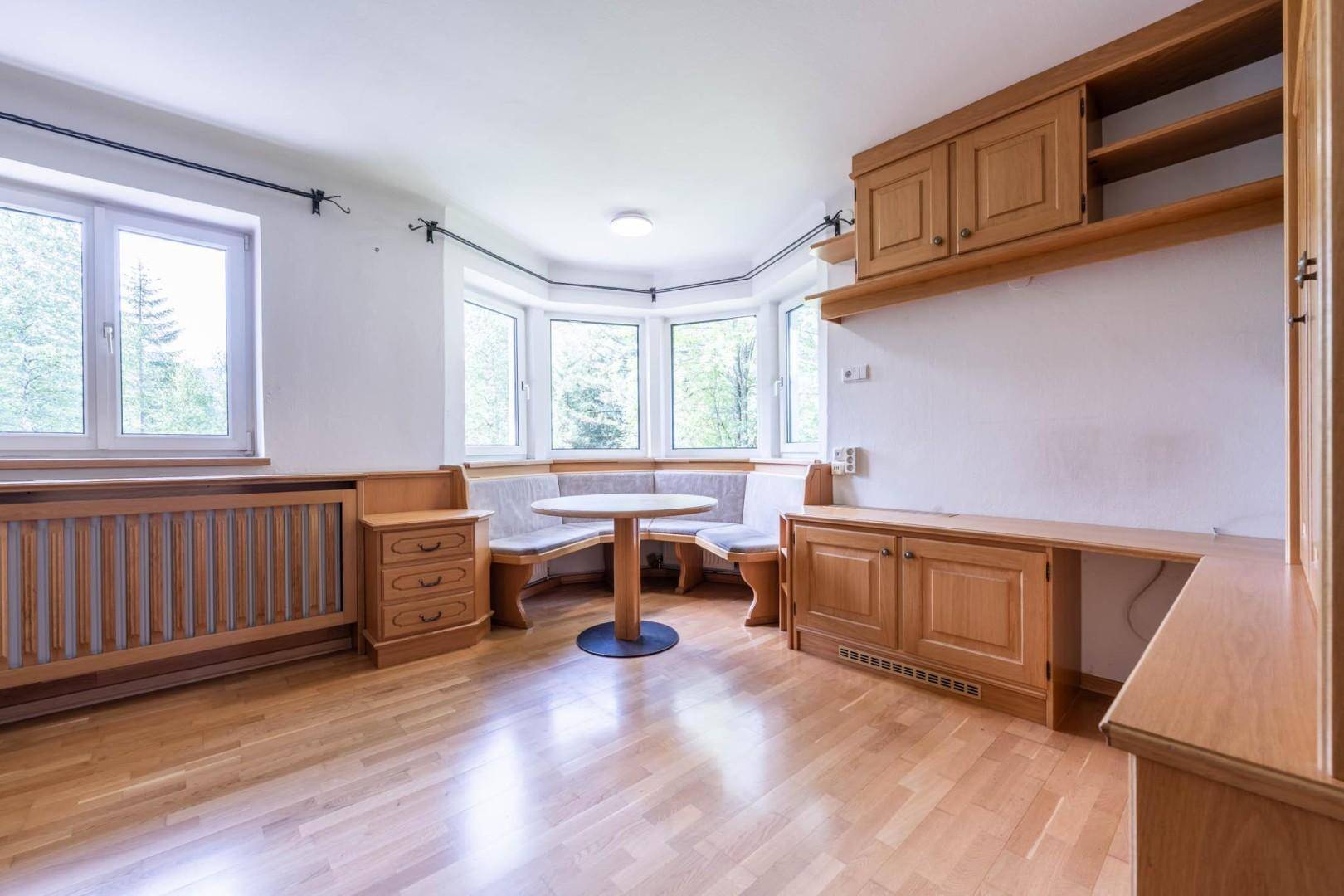 Heller Wohnbereich mit Holzboden, Einbaumöbeln und einer gemütlichen Sitzecke am großen Erkerfenster.