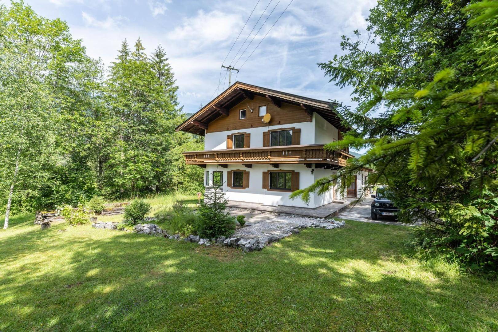 Traditionelles Haus mit Holzbalkon und grüner Rasenfläche, umgeben von Bäumen und Natur.