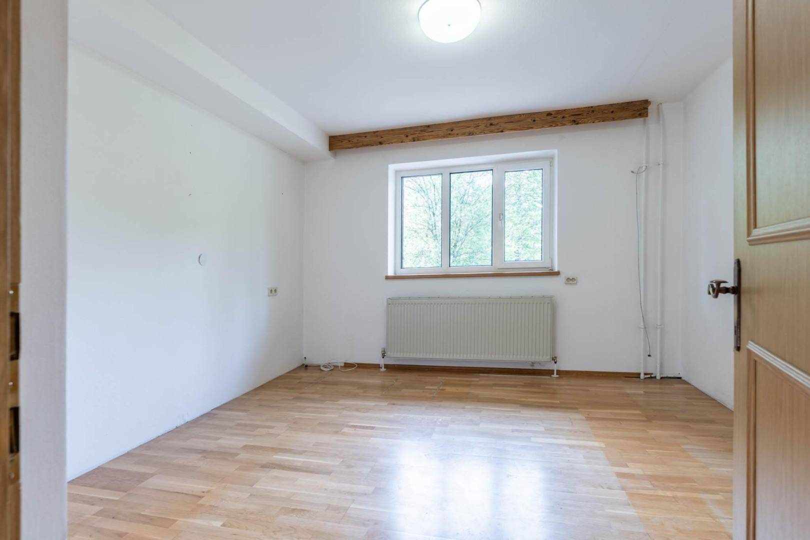 Helles Schlafzimmer mit Holzboden, großem Fenster und sichtbarem Deckenbalken, bereit zur Einrichtung.