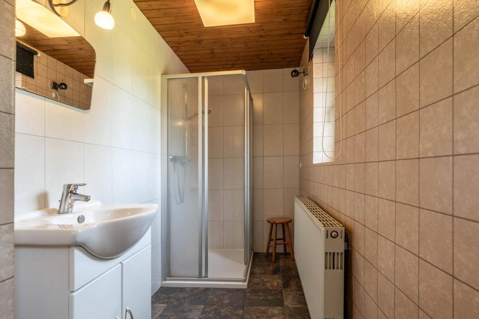 Funktionales Badezimmer mit Duschkabine, Waschbecken und hellen Fliesen, sowie Holzdecke.