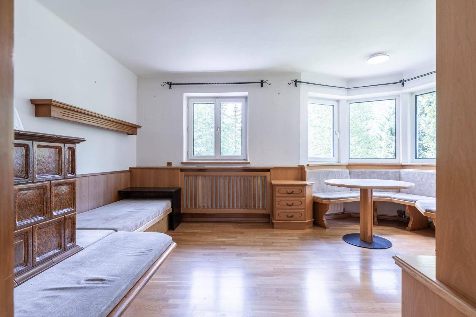 Gemütlicher Wohnbereich mit traditionellem Kachelofen, Holzboden und einer Sitzbank am Erkerfenster.