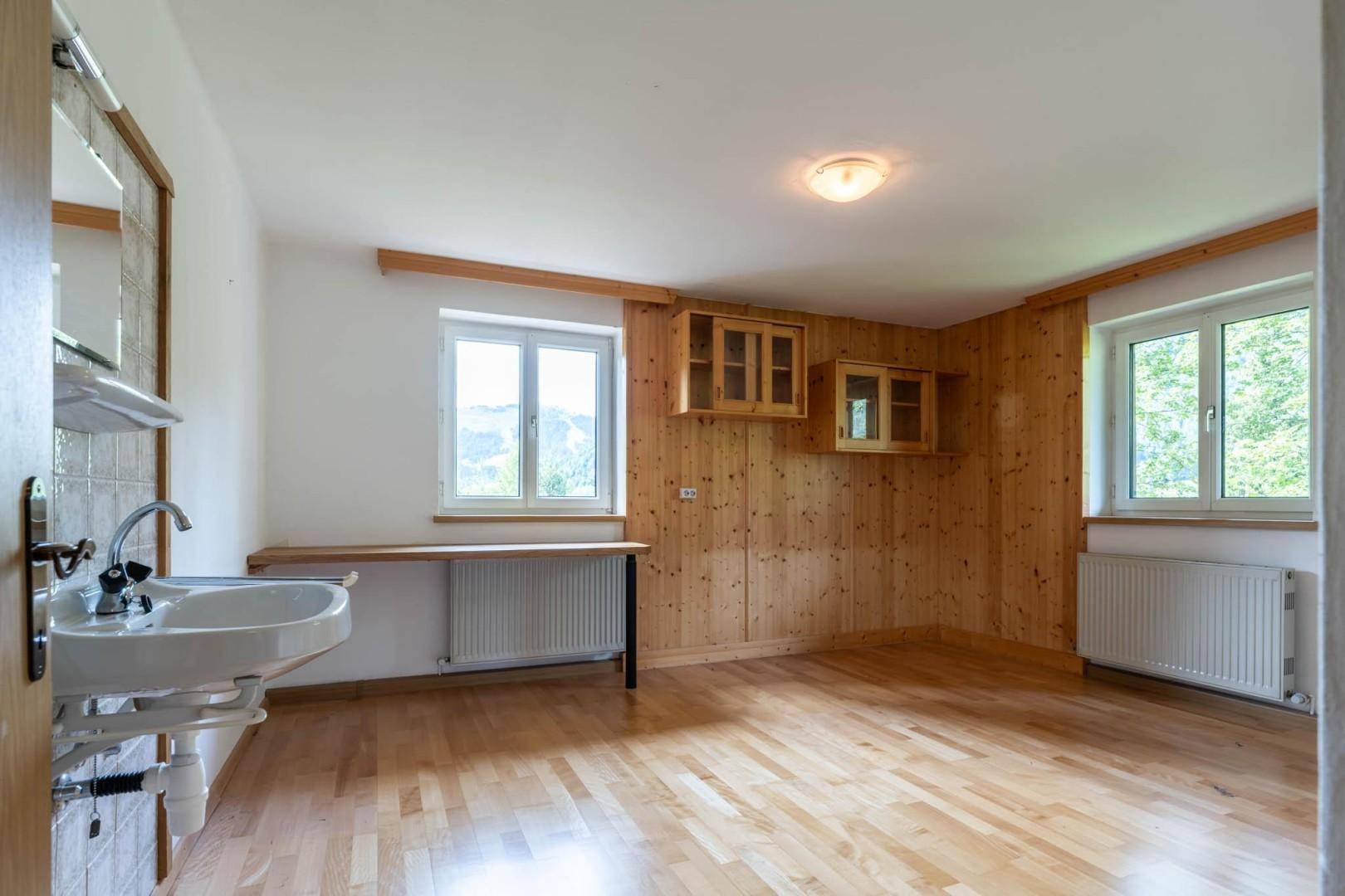 Geräumiges Zimmer mit Holzboden, Holzvertäfelung und Waschbecken, ideal als Gästezimmer oder Schlafzimmer.