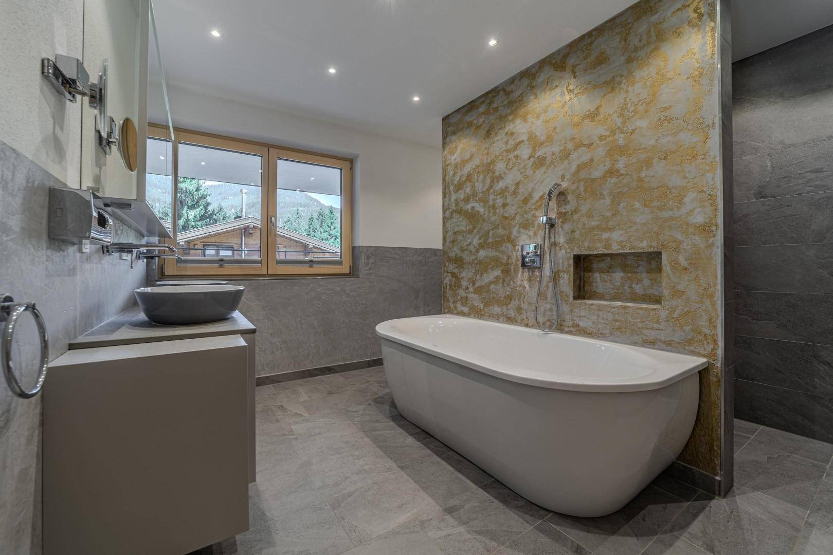 Luxuriöses Badezimmer mit freistehender Badewanne, separater Dusche und Fenster mit Bergblick.