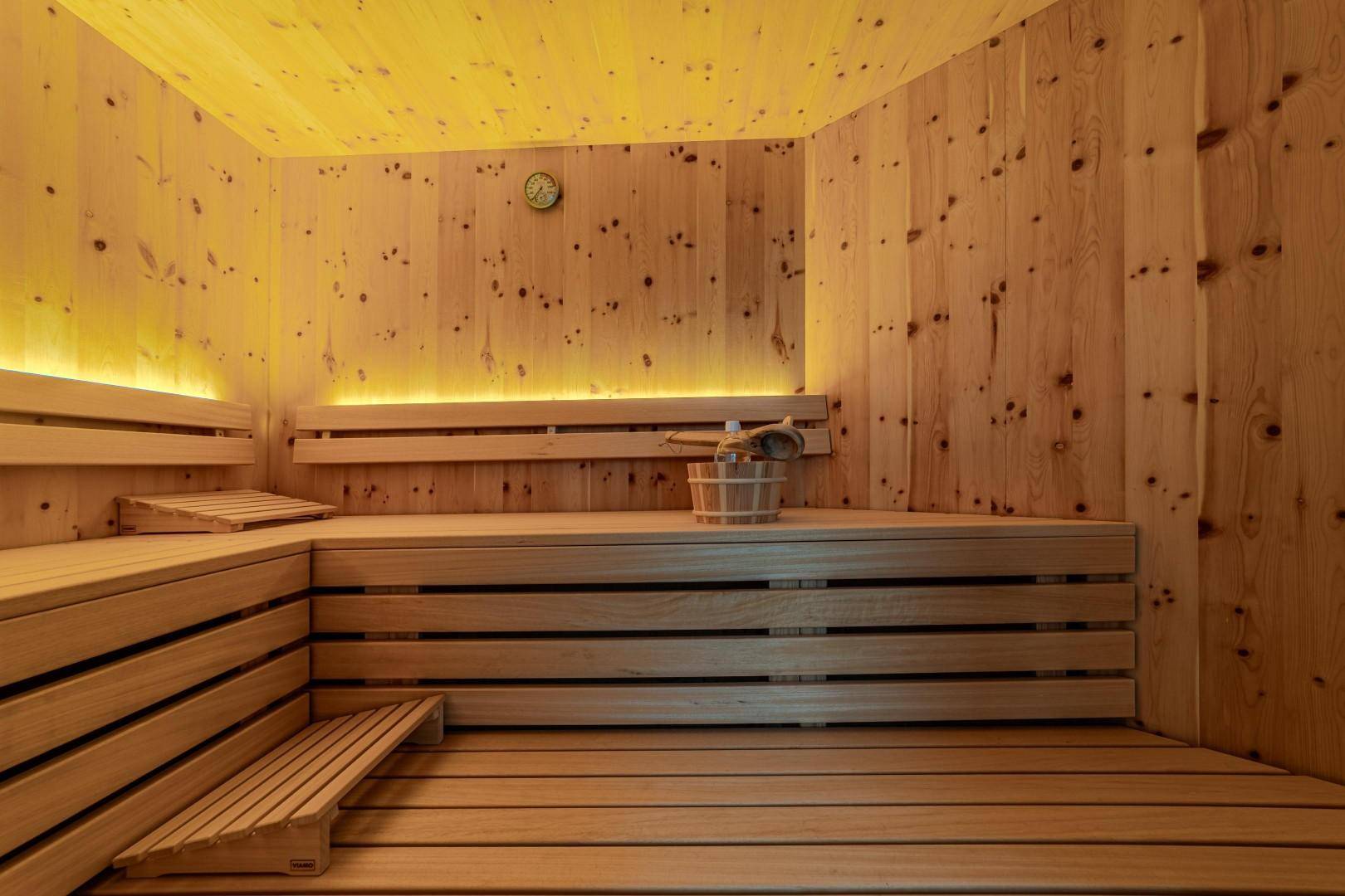 Helle Holzsauna mit mehrstufigen Bänken, indirekter Beleuchtung und traditionellem Aufgusseimer.