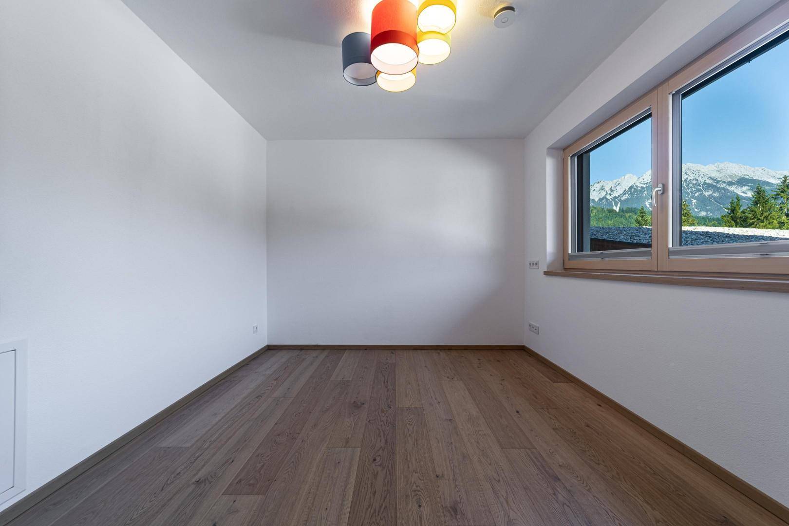 Unmöbliertes Zimmer mit Holzboden und Fenster, das einen beeindruckenden Bergblick bietet.