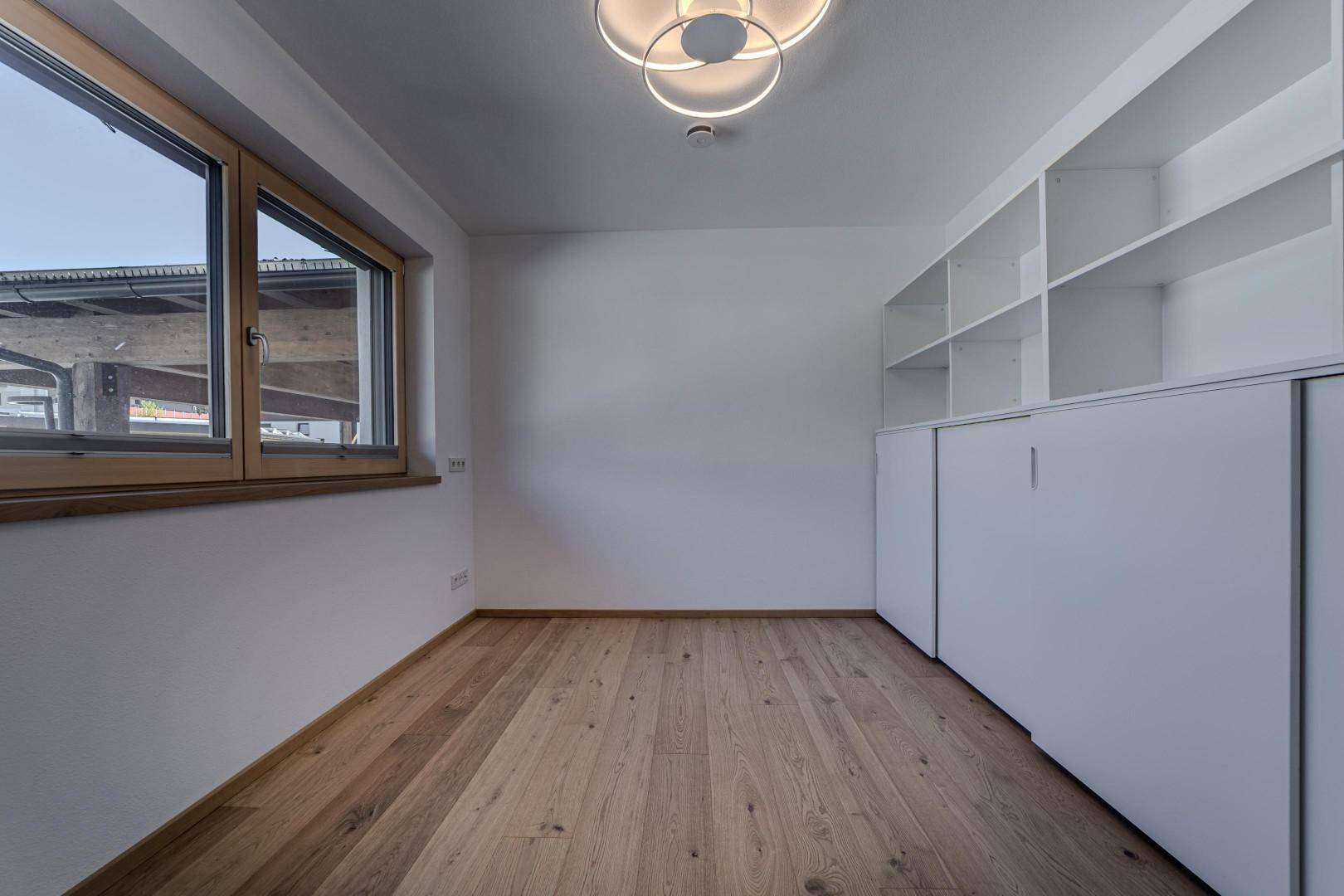 Helles Zimmer mit Holzboden und integrierten Regalen, ideal als Büro oder Gästezimmer.