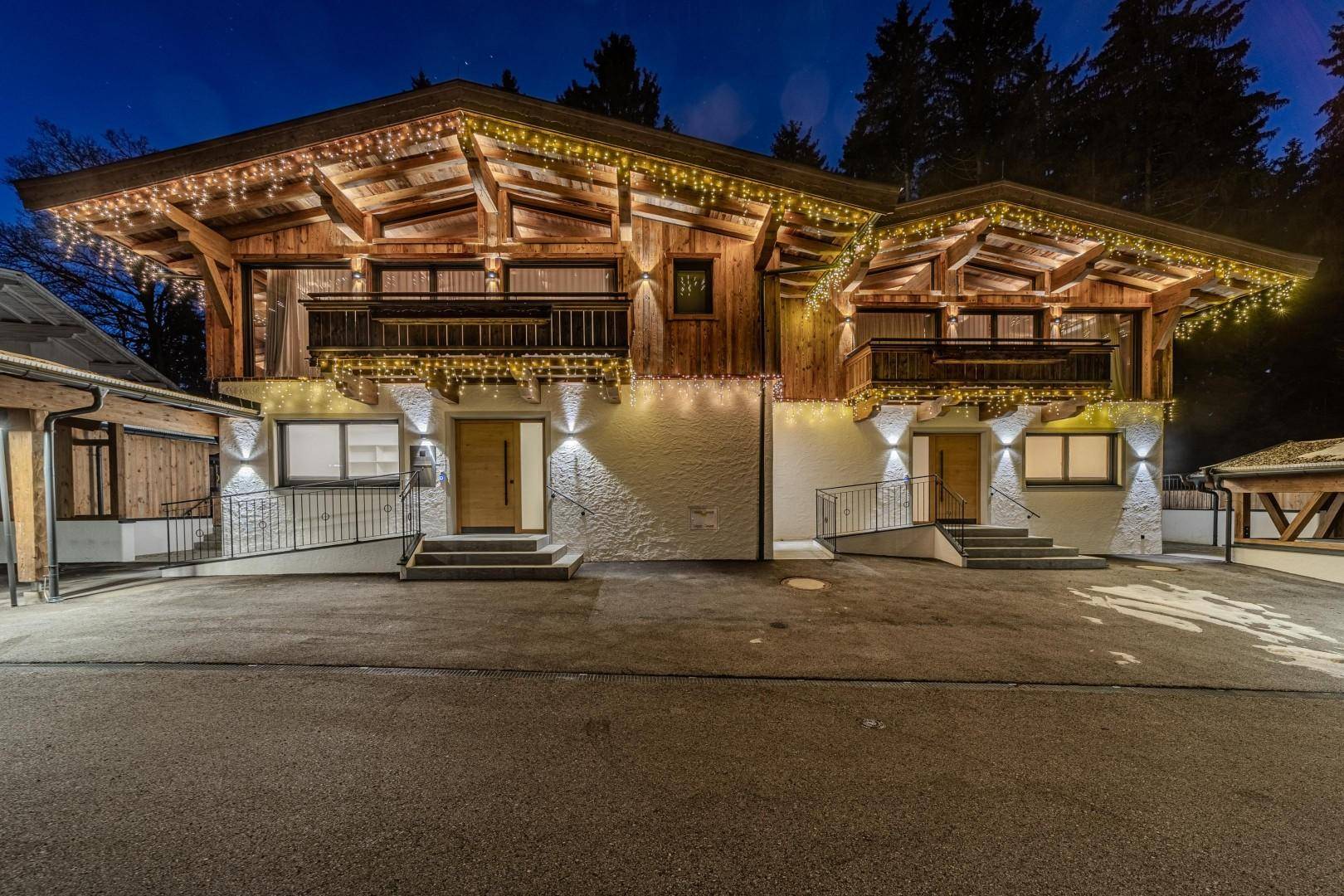 Beleuchtete Fassade eines modernen Chalets bei Nacht, mit Holzbalkonen und festlicher Dekoration.