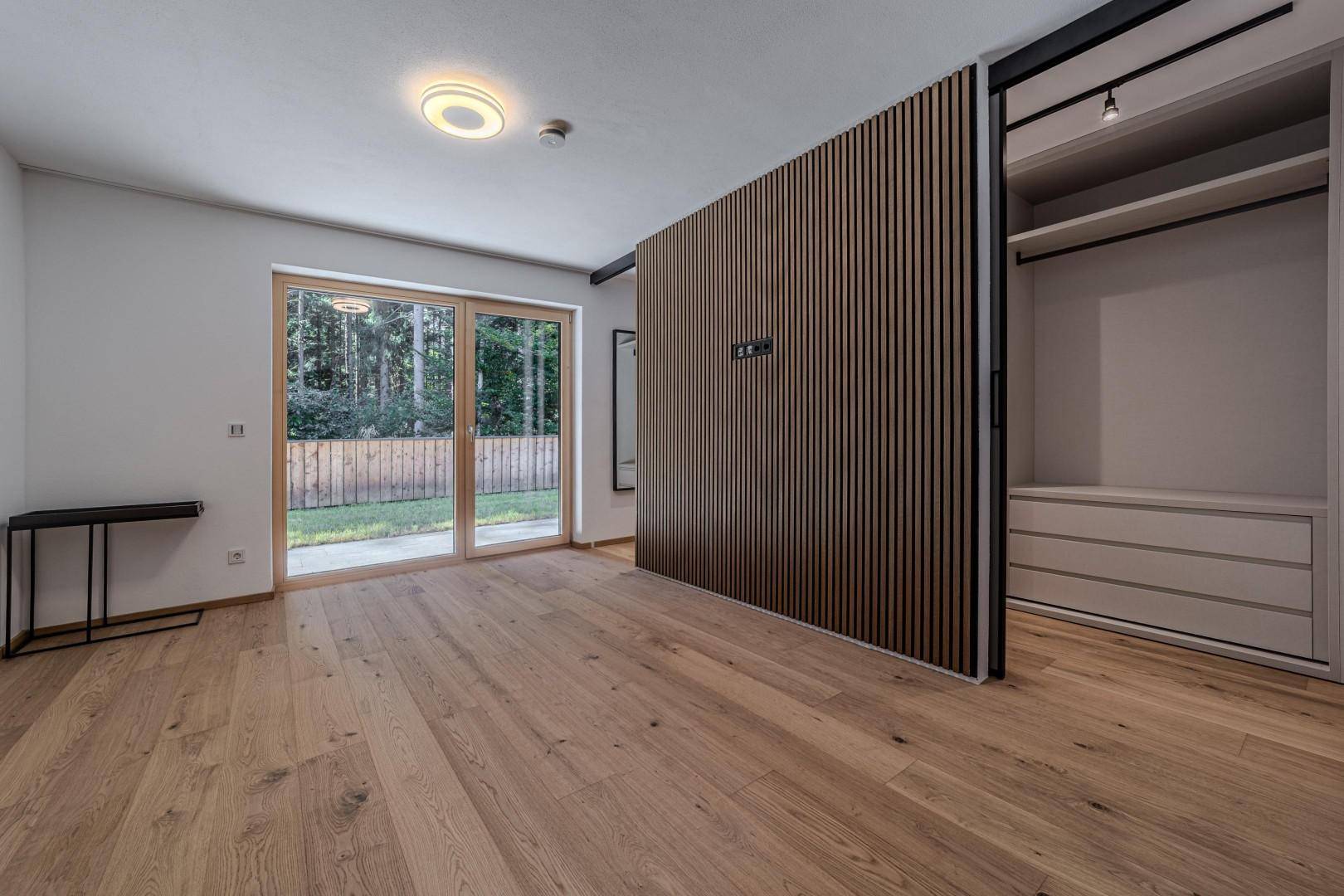 Schlafzimmer mit Holzboden, Schiebetür zum begehbaren Kleiderschrank und Zugang zum Garten.