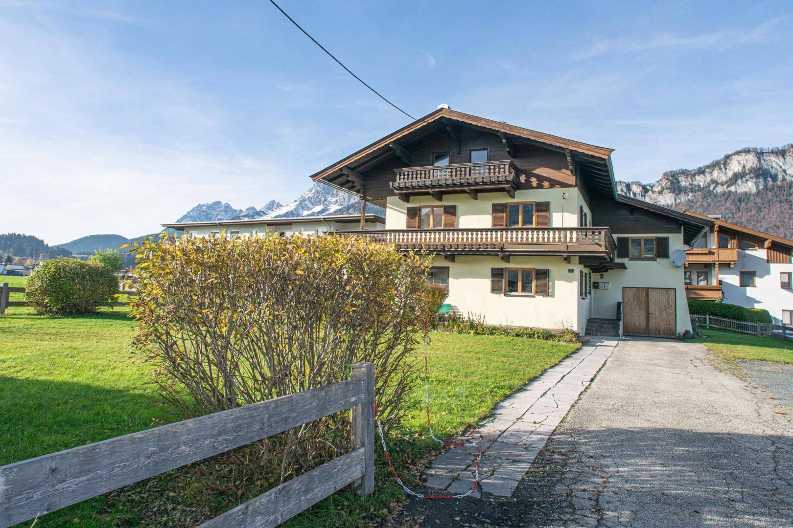 Traditionelles Haus mit Balkonen, umgeben von einem Garten und einer Zufahrt, mit Bergblick.