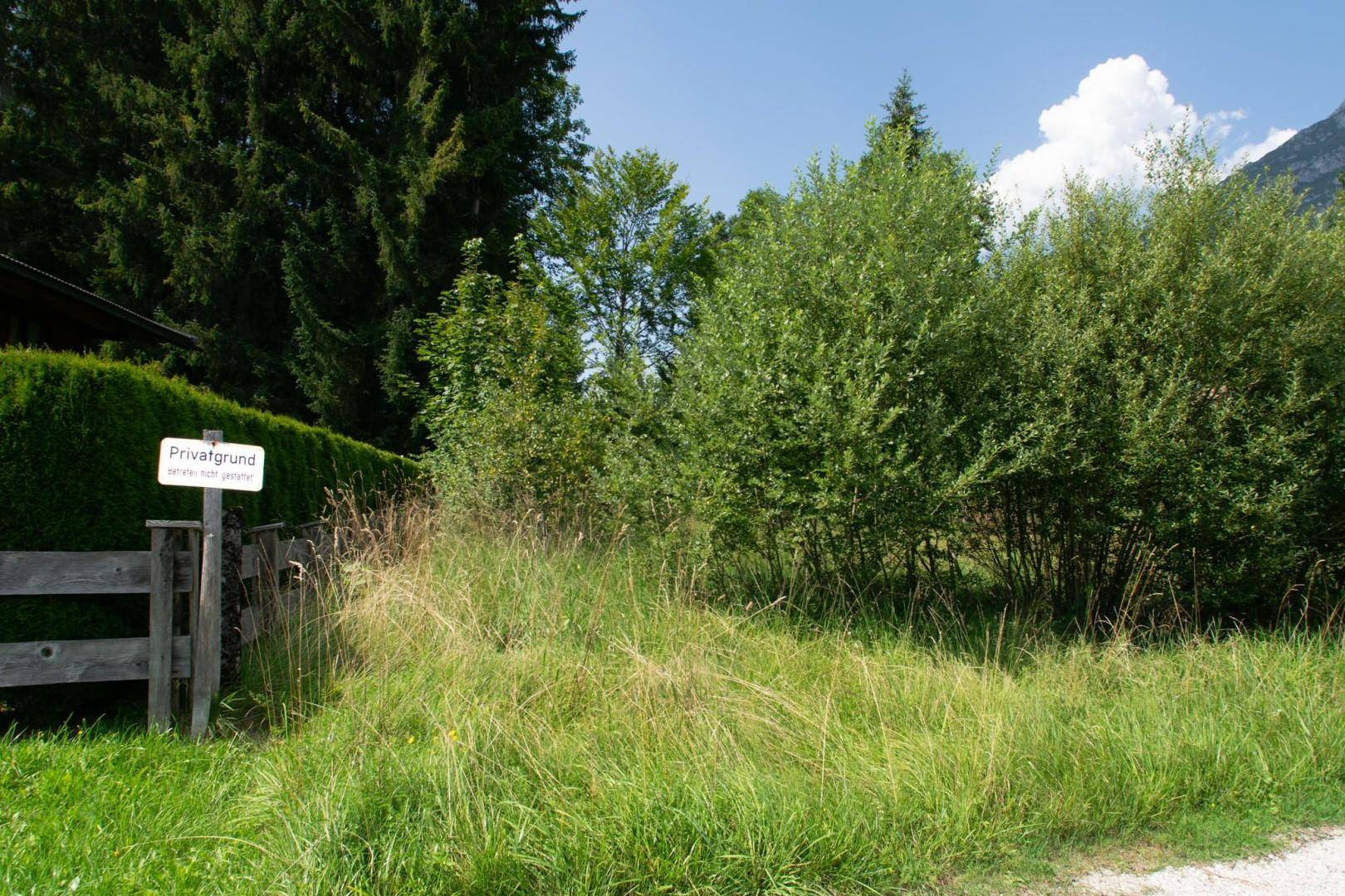 Wild bewachsenes Grundstück mit Büschen, einem Holzzaun und einem "Privatgrund"-Schild.