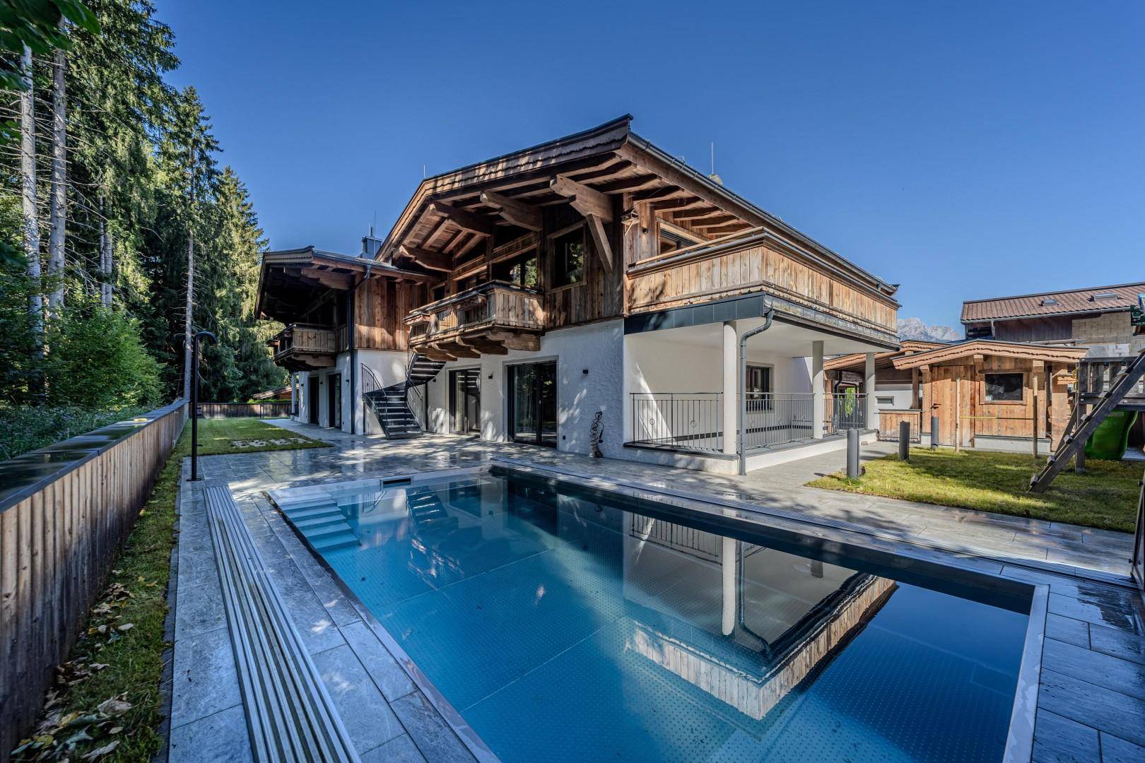 Luxuriöses Chalet mit großem Außenpool und weitläufiger Terrasse, umgeben von dichtem Wald.