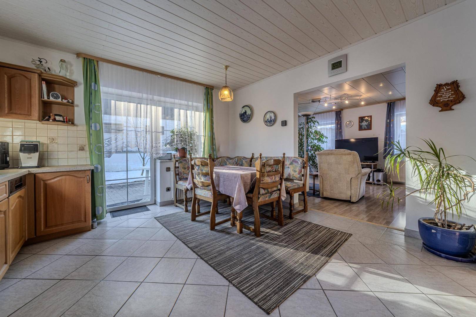 Helle Wohnküche mit Essbereich, Fliesenboden und Zugang zum Garten, offen zum Wohnzimmer.
