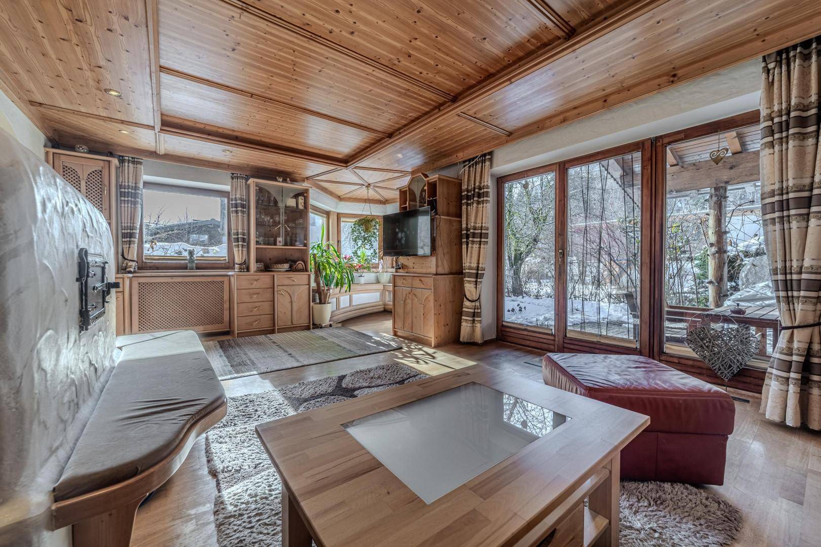 Traditionelles Wohnzimmer mit Kachelofen, Holzboden und großen Fenstern zum Garten.