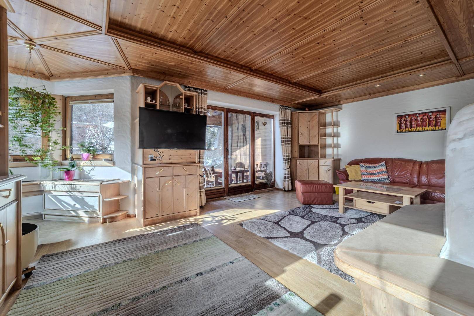Heller Wohnbereich mit Holzbalkendecke, bequemer Ledercouch und Zugang zur Terrasse.