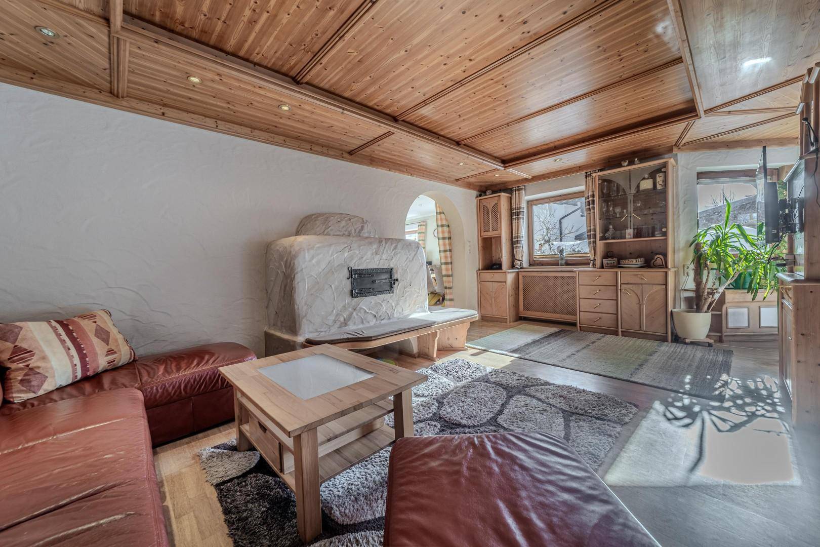 Rustikales Wohnzimmer mit großem Kachelofen, Ledersofa und Holzbalkendecke.