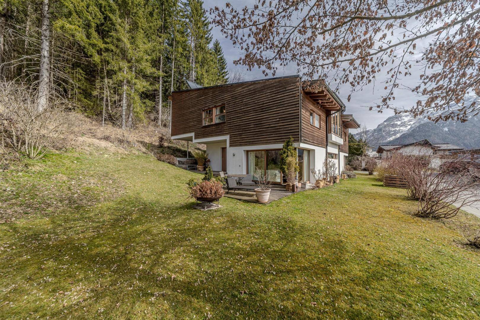 Charmantes Haus mit Holzfassade, umgeben von einem grünen Garten und Bergblick.