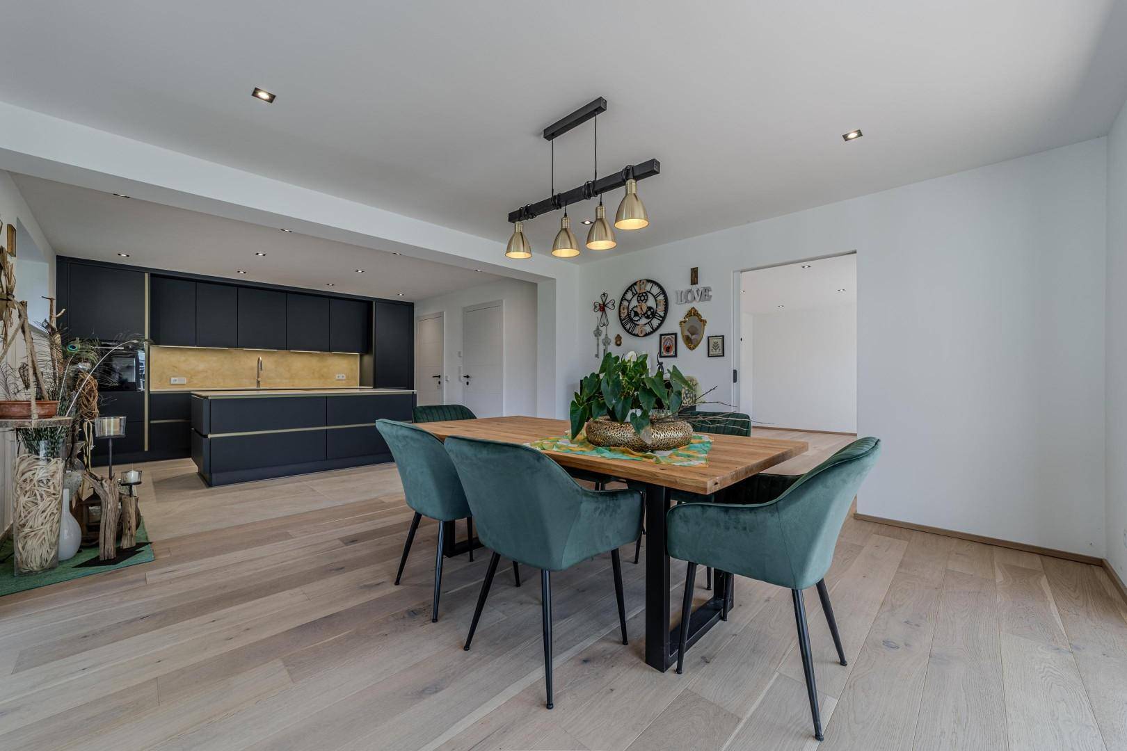 Geräumiger Essbereich mit Holztisch und grünen Stühlen, offen zur modernen Küche mit dunklen Fronten.
