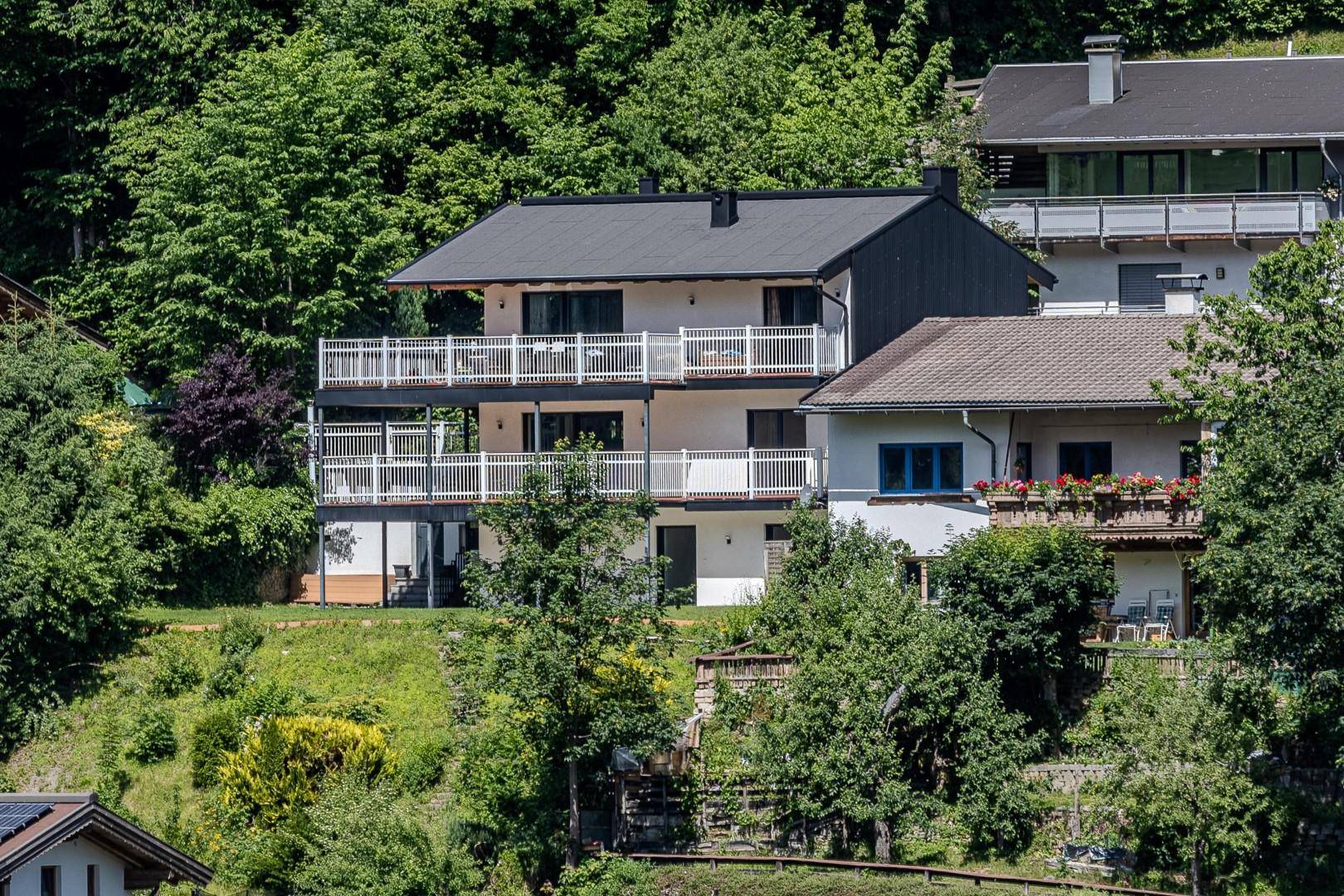 Mehrstöckiges Wohnhaus in Hanglage mit mehreren Balkonen und umgeben von üppiger grüner Vegetation.