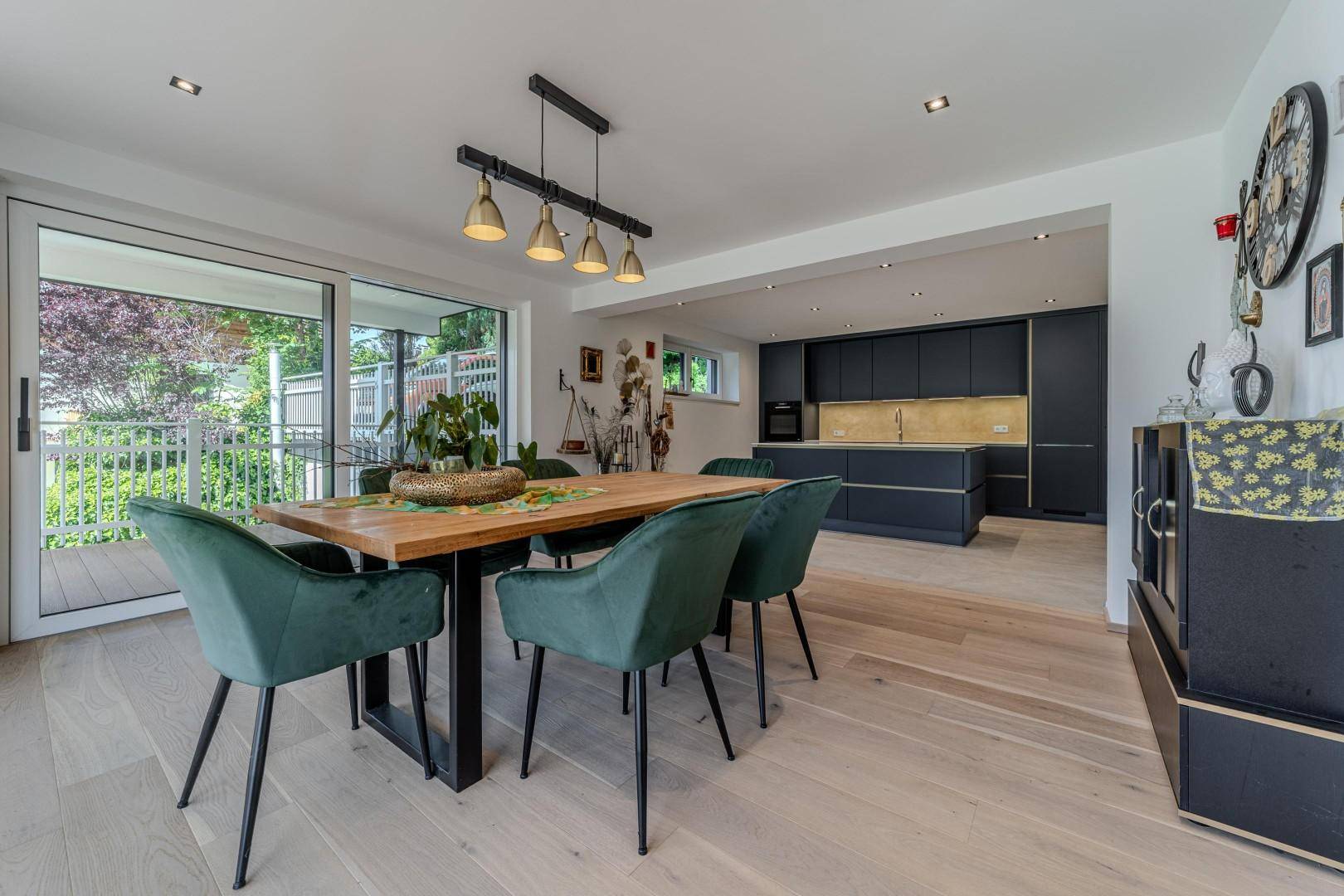 Heller Essbereich mit Holztisch und grünen Stühlen, offen zur modernen Küche und mit Zugang zur Terrasse.