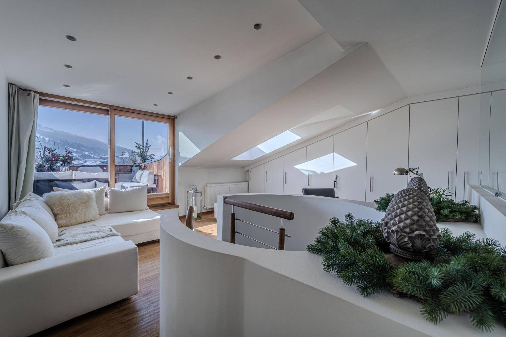 Gemütliches Wohnzimmer im Dachgeschoss mit Zugang zum Balkon und Panoramablick auf die Berge.