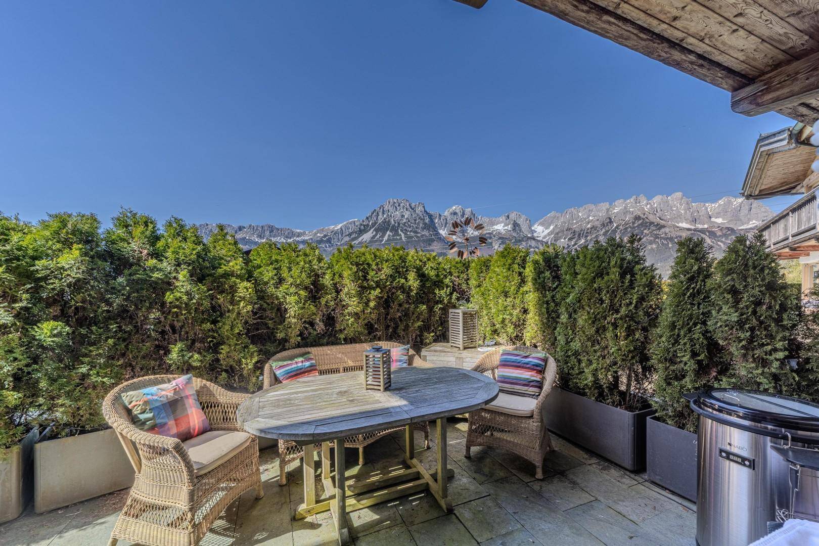 Gemütliche Terrasse mit Korbmöbeln, umgeben von hohen Hecken und einem weiten Bergblick.