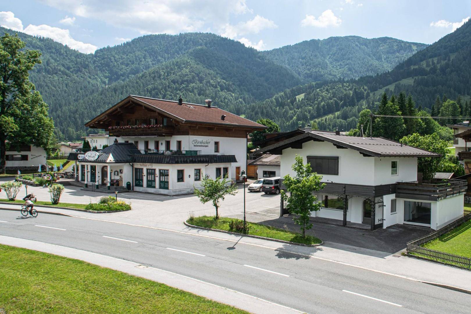 Zwei Gebäude mit traditioneller und moderner Architektur, umgeben von Bergen und einer Straße.