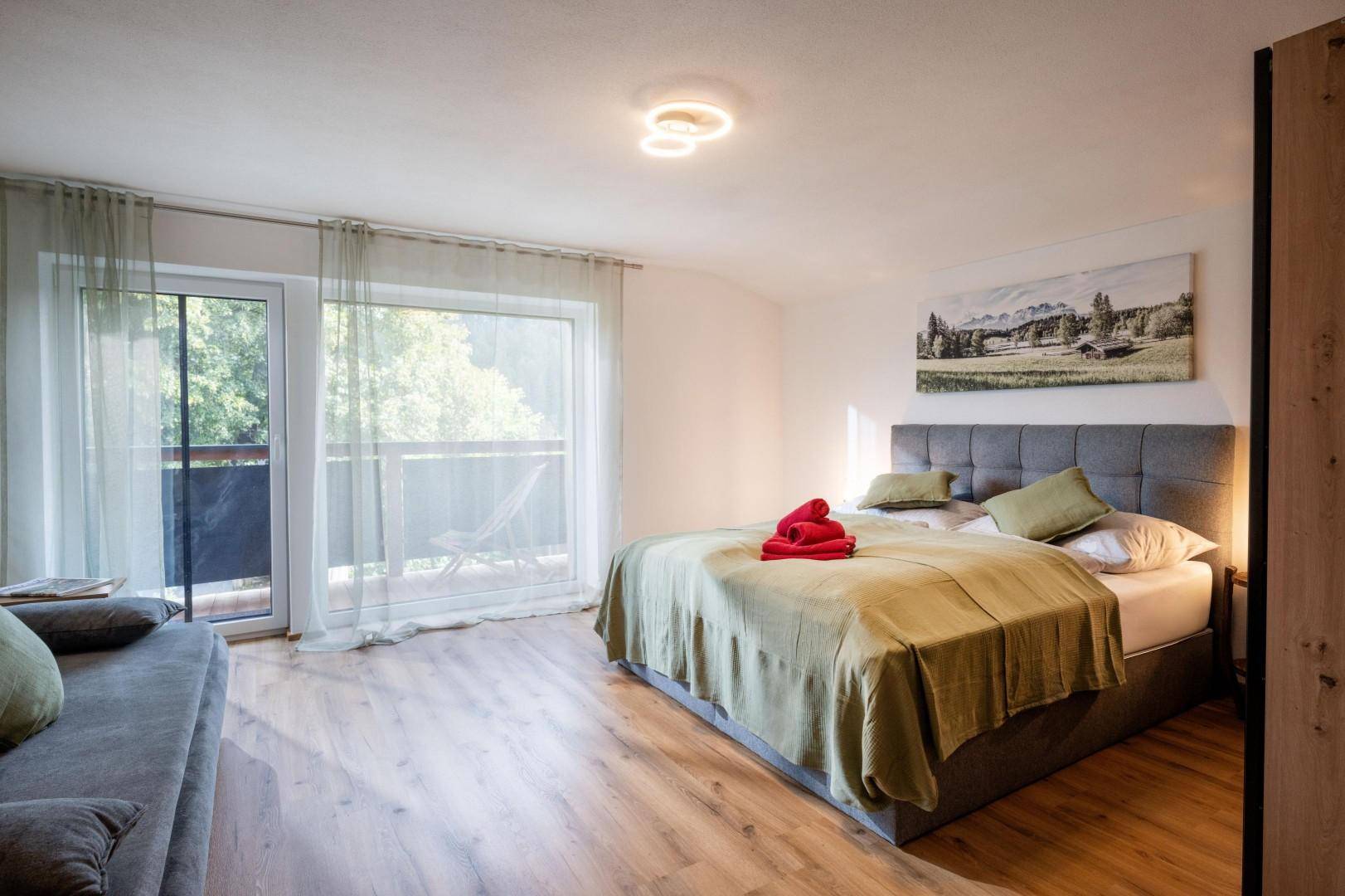 Gemütliches Schlafzimmer mit Doppelbett, Sofa und direktem Zugang zum sonnigen Balkon.