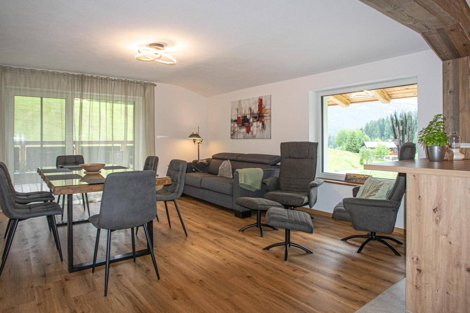 Lichtdurchfluteter Wohn- und Essbereich mit großen Fenstern, Holzboden und Zugang zum Balkon.