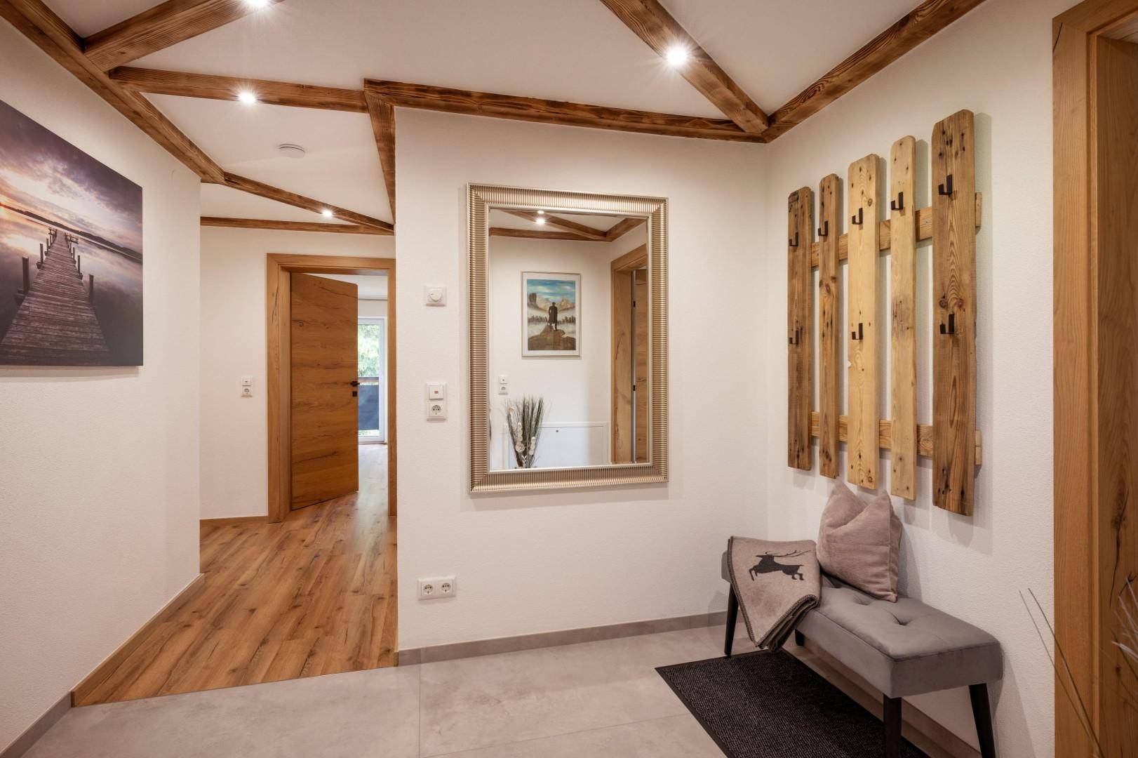 Einladender Flur mit Holzbalken, Garderobe und Spiegel, der zu den Wohnbereichen führt.