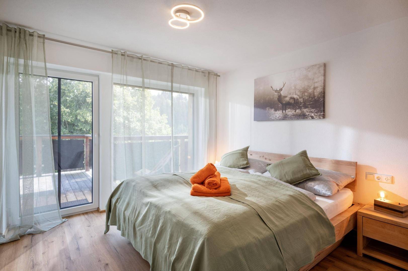 Helles Schlafzimmer mit Holzbett, Laminatboden und großem Fenster mit Blick ins Grüne.