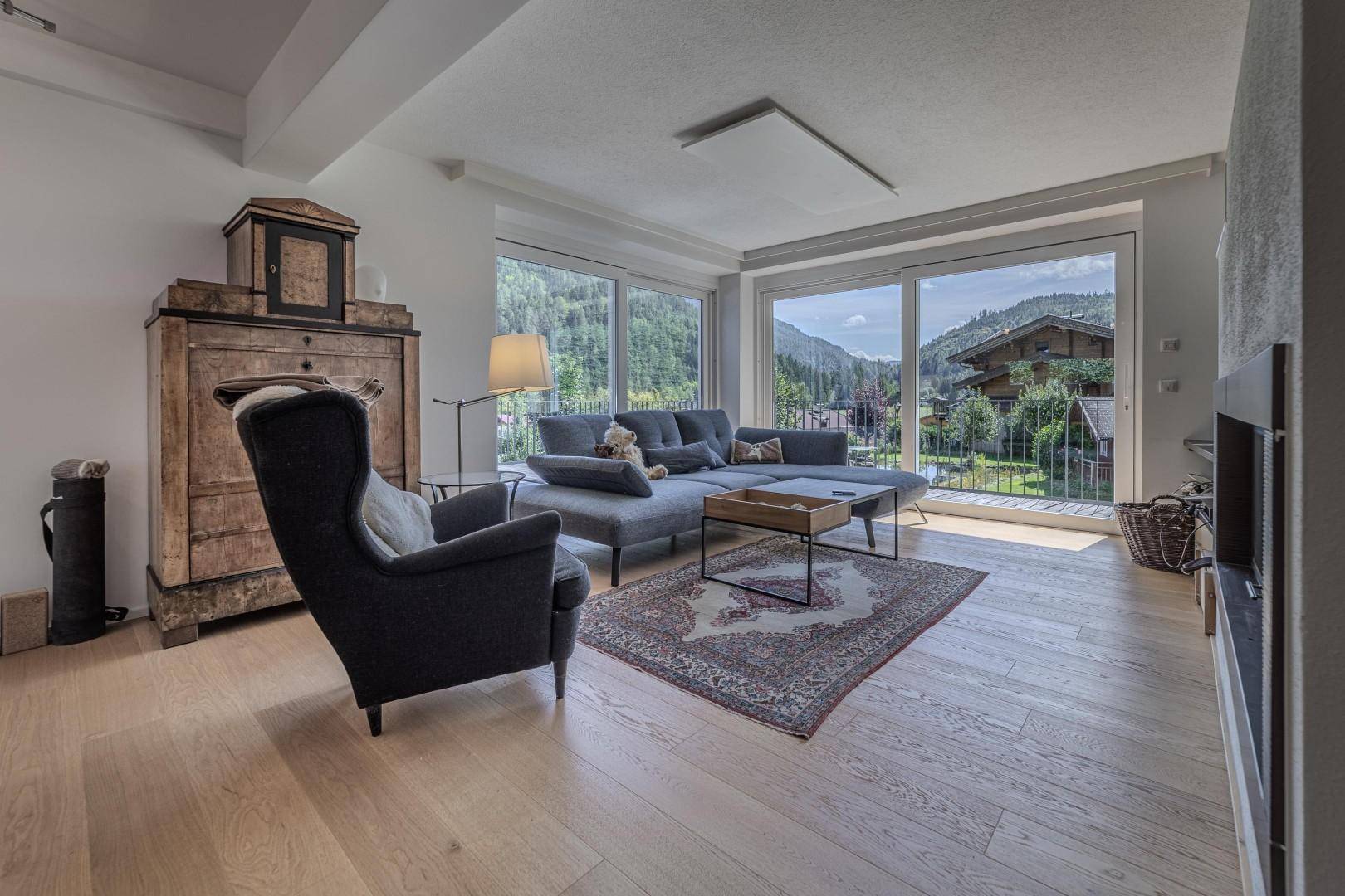 Gemütlicher Wohnbereich mit Sofa, Sessel und Panoramafenstern mit Bergblick.