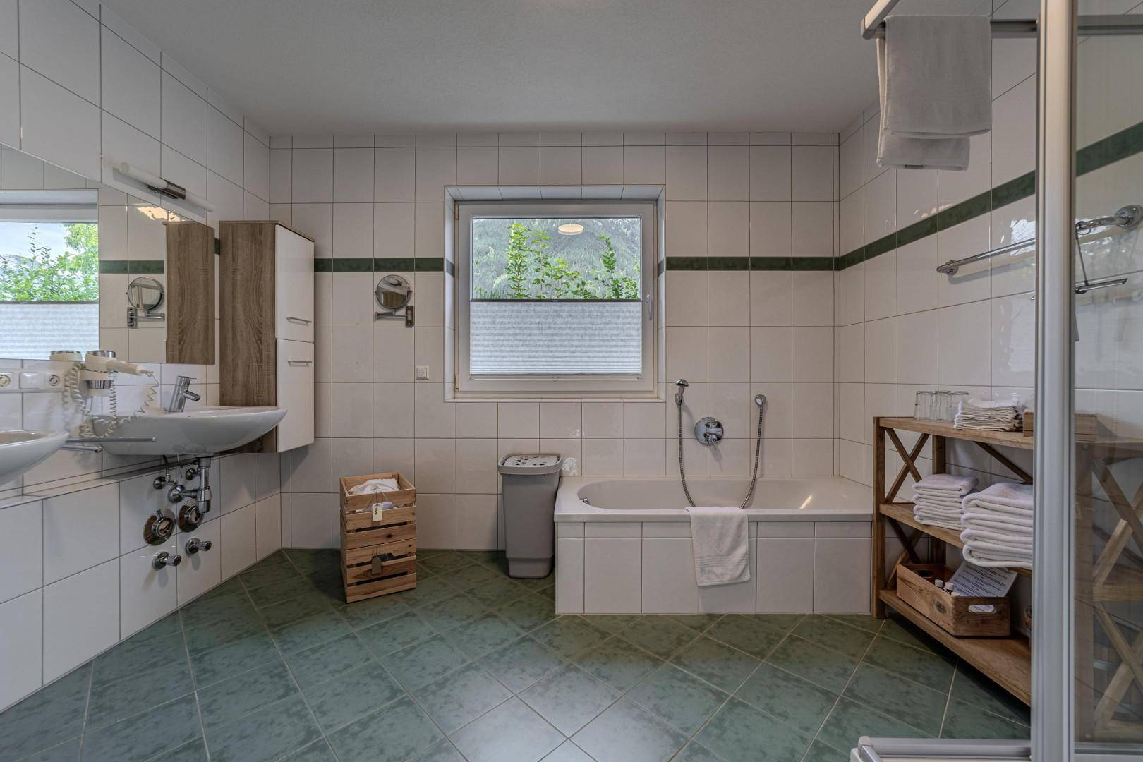 Geräumiges Badezimmer mit Badewanne, Dusche, Doppelwaschbecken und Fenster.