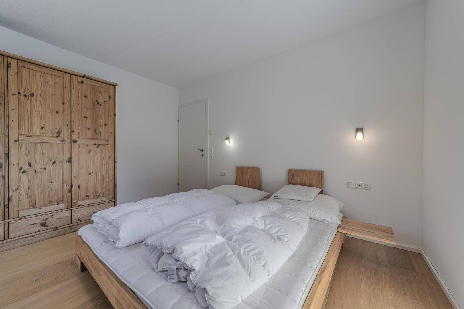 Schlafzimmer mit Holzbett, weiß gestrichenen Wänden und großem Holzschrank.