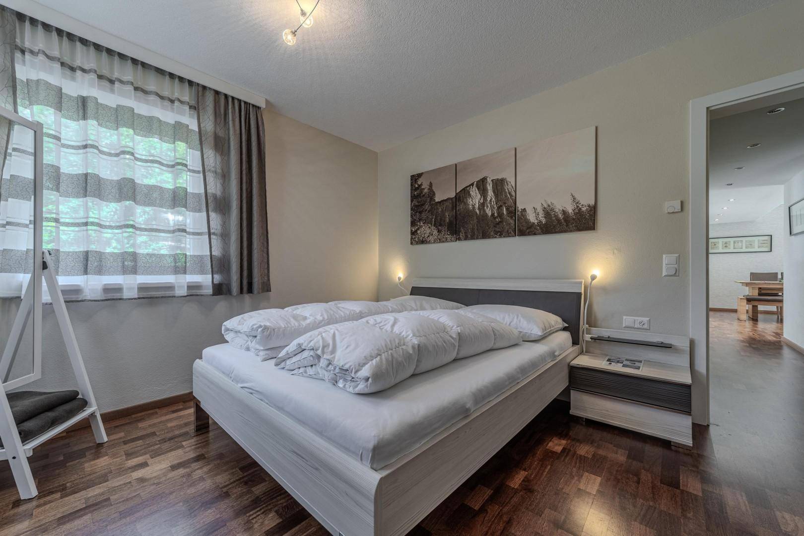 Schlafzimmer mit Holzboden, großem Bett und einem Blick in den angrenzenden Flur.