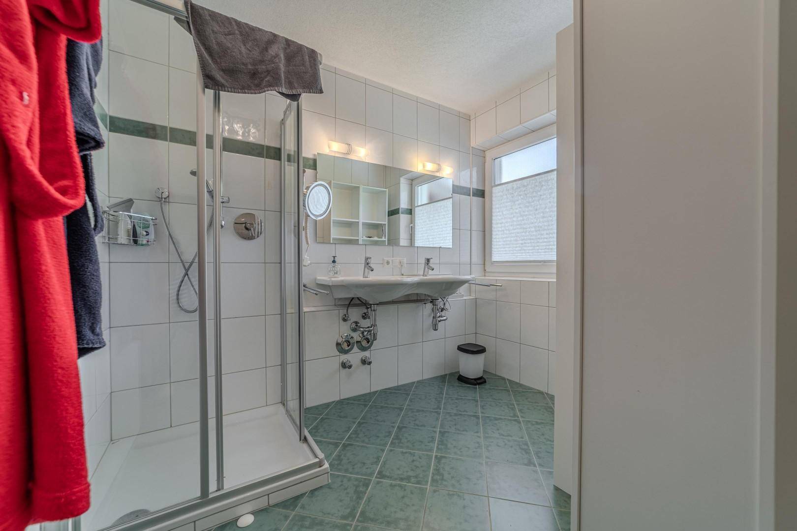 Badezimmer mit Duschkabine, Doppelwaschbecken und Fenster für Tageslicht.