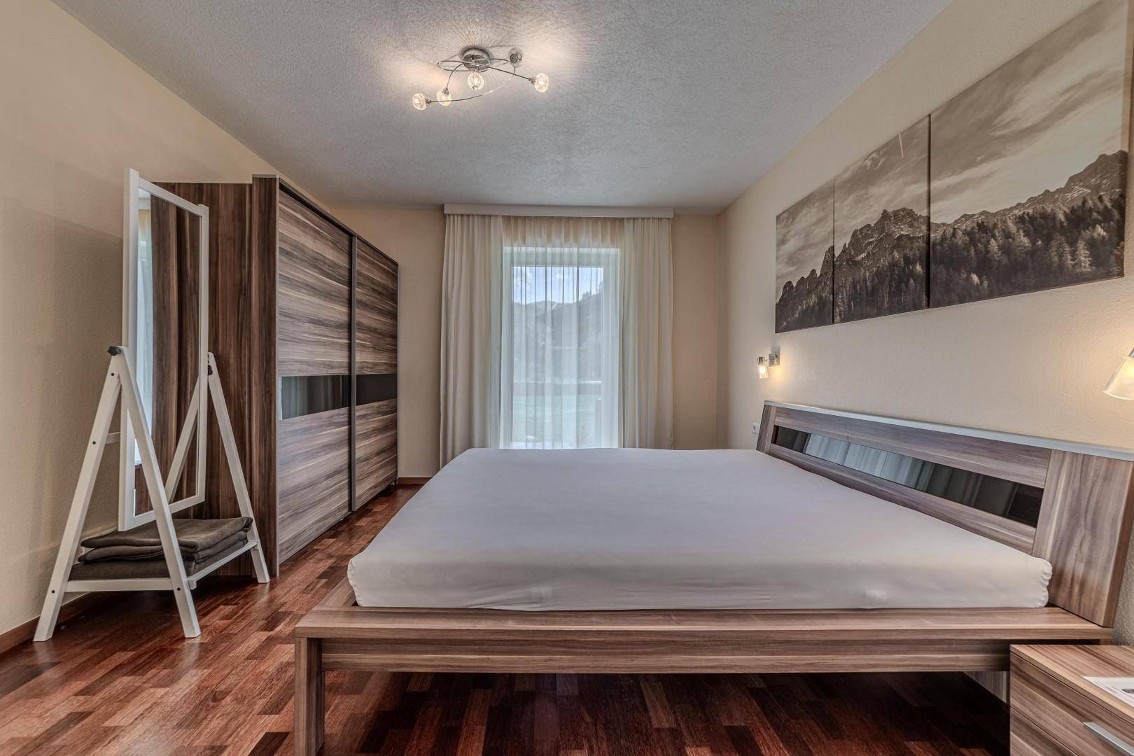 Schlafzimmer mit Doppelbett, Holzschrank und großem Fenster mit Blick ins Grüne.