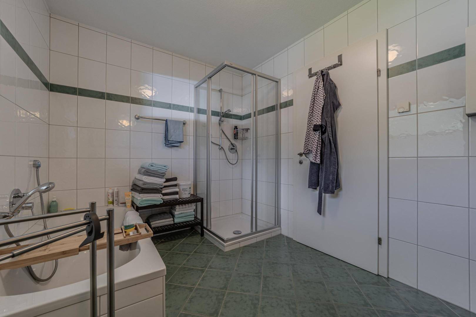 Geräumiges Badezimmer mit Duschkabine, Badewanne und grünen Bodenfliesen.