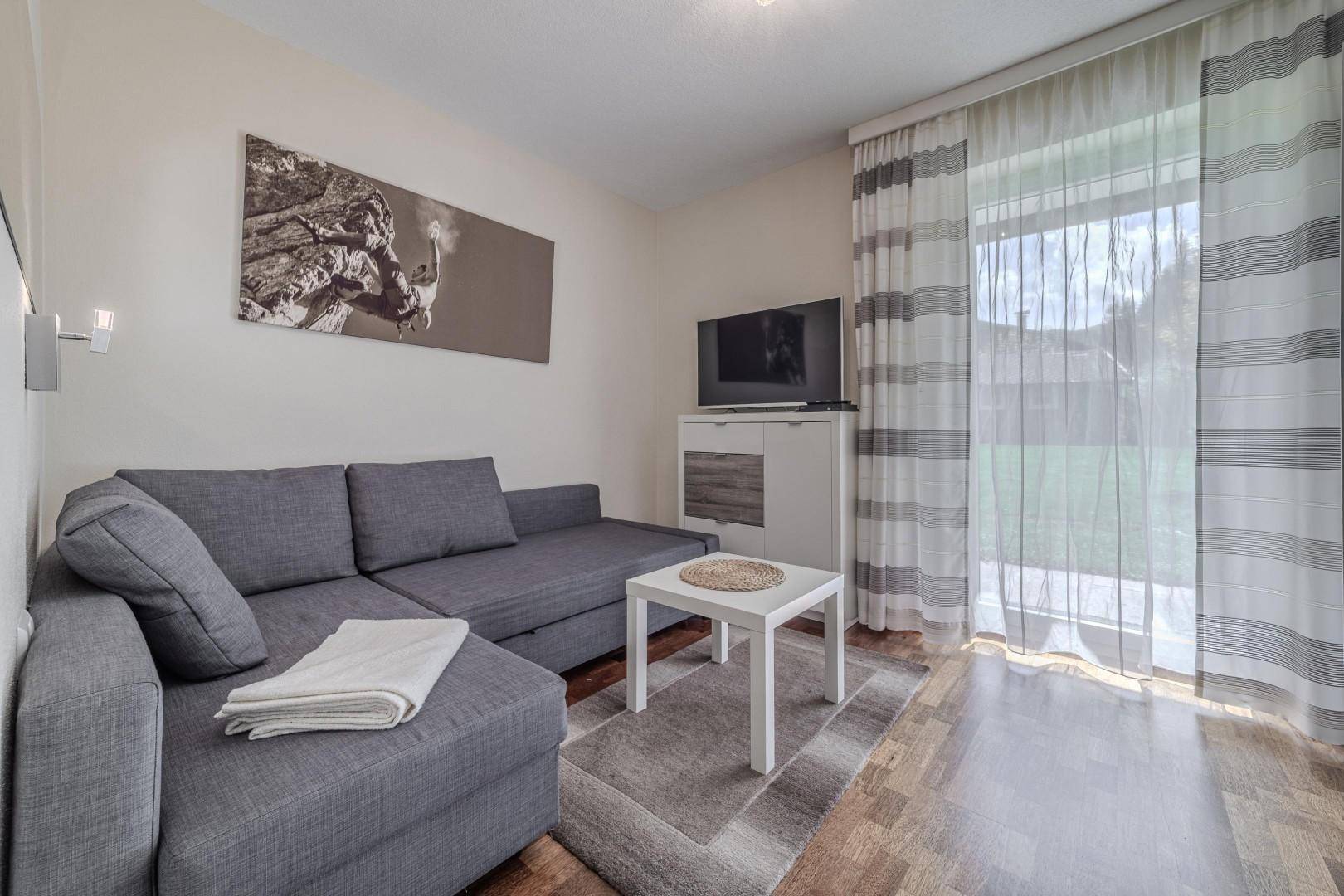 Gemütliches Wohnzimmer mit grauem Sofa, Couchtisch und großen Fenstern.