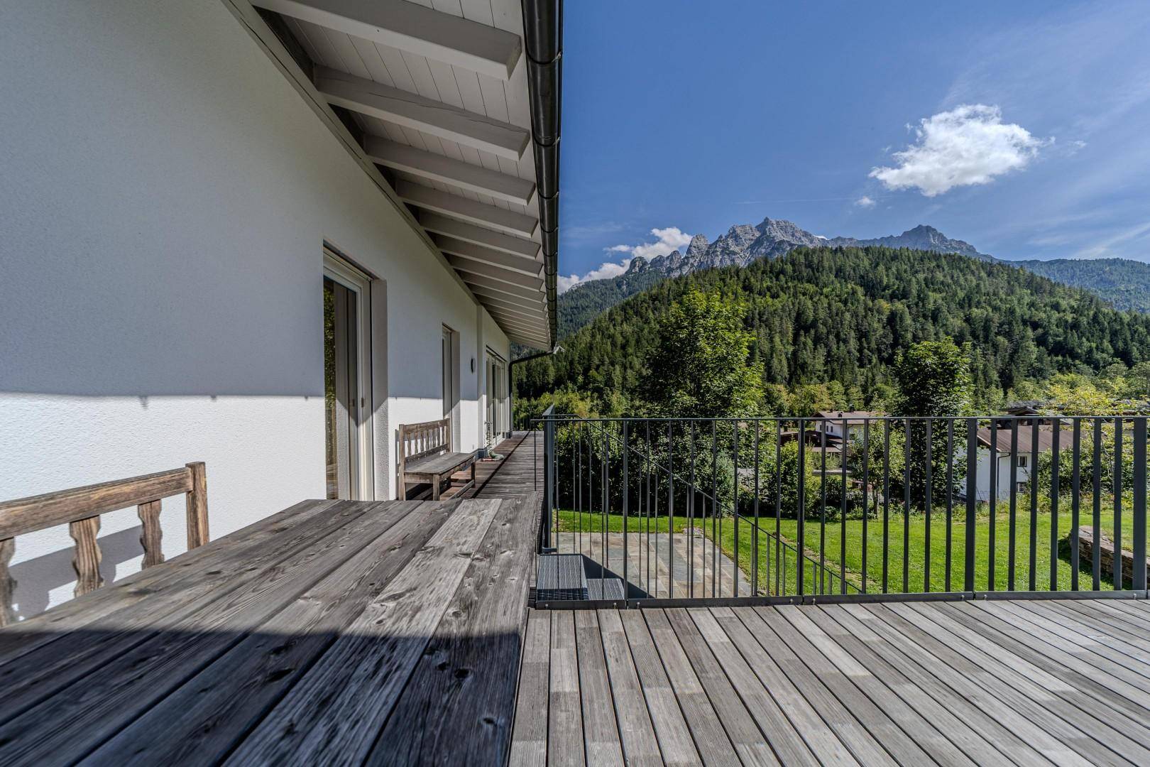 Langer Holzbalkon mit Metallgeländer und Panoramablick auf die bewaldeten Berge unter blauem Himmel.