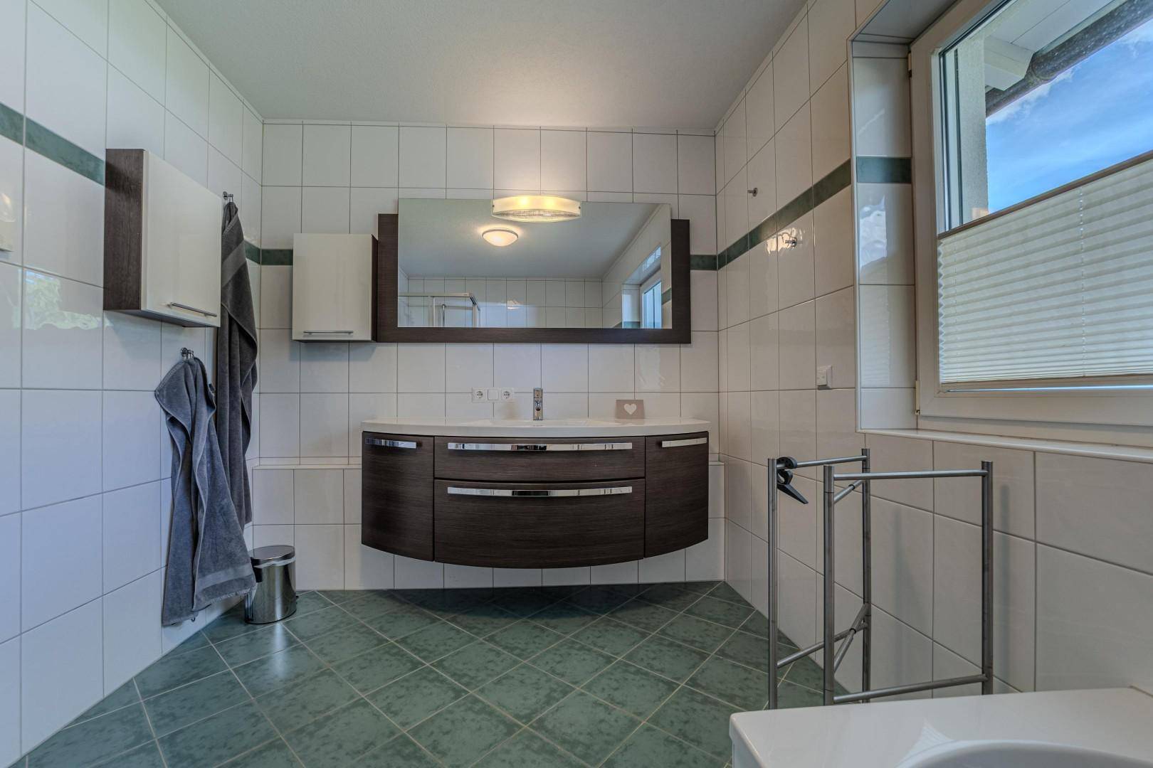 Badezimmer mit grünen Bodenfliesen, modernem Waschtisch und großem Spiegel.
